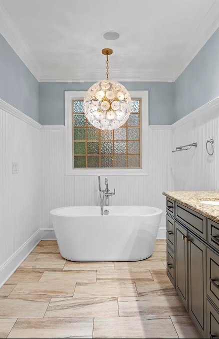 Bathroom with a white soaking tub, gold chandelier, and wood-look tile floor.