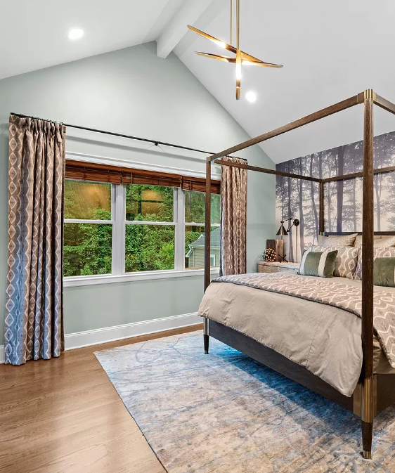 Bedroom with canopy bed, patterned rug, curtains, and window overlooking trees.