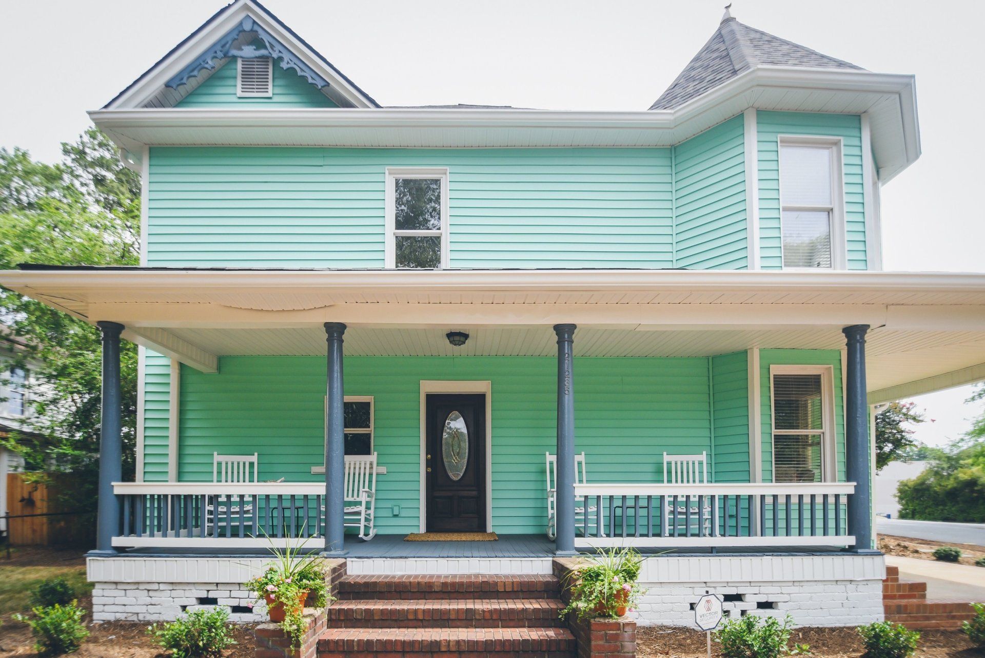 Two-story teal house with porch and dark door, white trim, and brick steps.