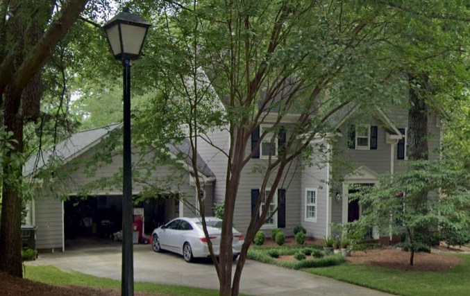 House with a gray exterior, attached garage, and white car parked in the driveway, trees and greenery in front.