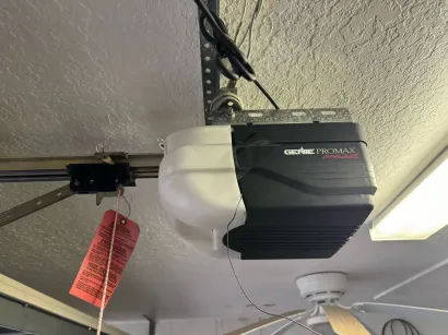 Garage door opener mounted on the ceiling with a red warning tag hanging from it.