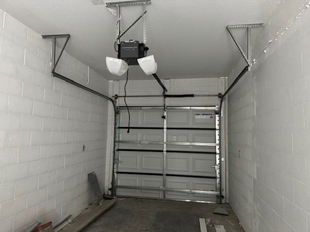 Garage interior with a closed white garage door, overhead opener, and exposed support beams.