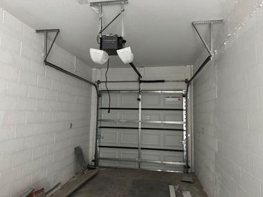 Garage interior with a closed white garage door, overhead opener, and exposed support beams.
