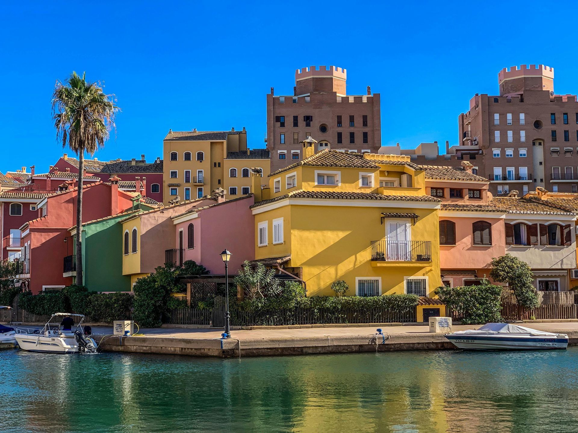 Blue ocean bay framed by green trees and cliffs under a sunny sky with white clouds; boats dot the water.