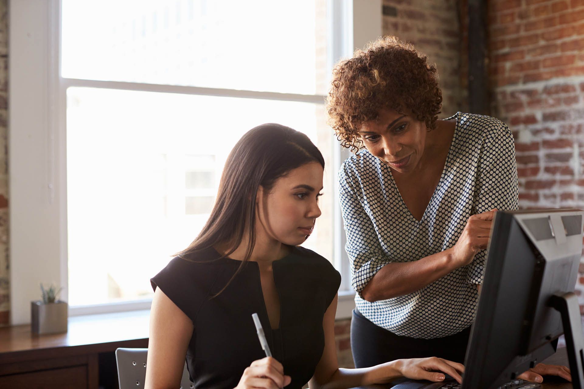 A woman is teaching another woman how to use a computer.