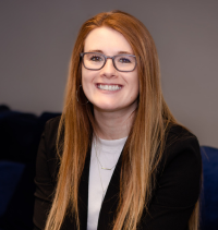 A woman wearing glasses and a black jacket is smiling for the camera.