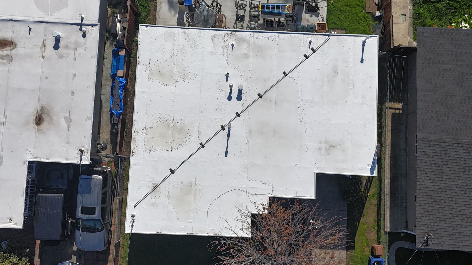 Overhead view of a white commercial flat roof with dirt and dark lines.