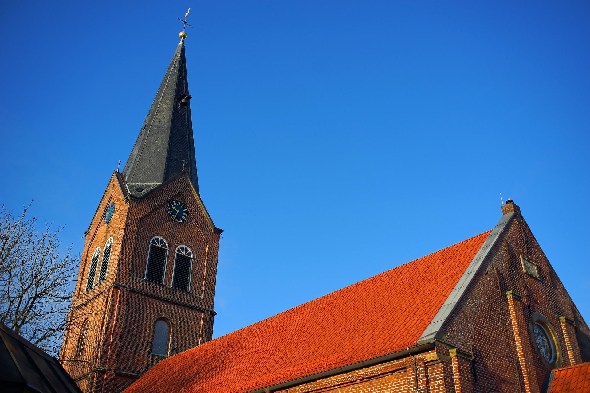 Brick church with red tiled roof and tall steeple against a clear blue sky.