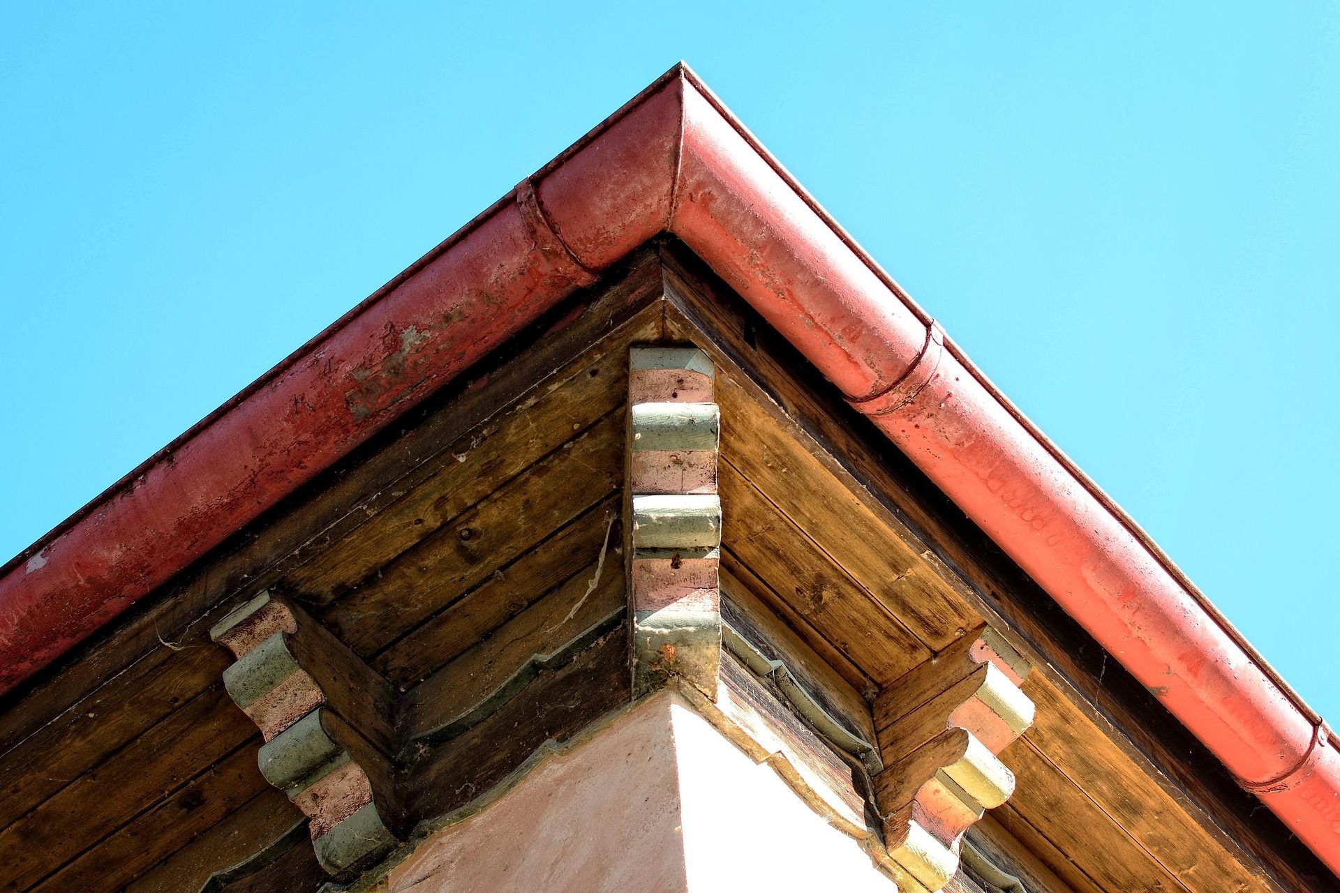 Corner of a building with red gutter, wooden trim, and blue sky.