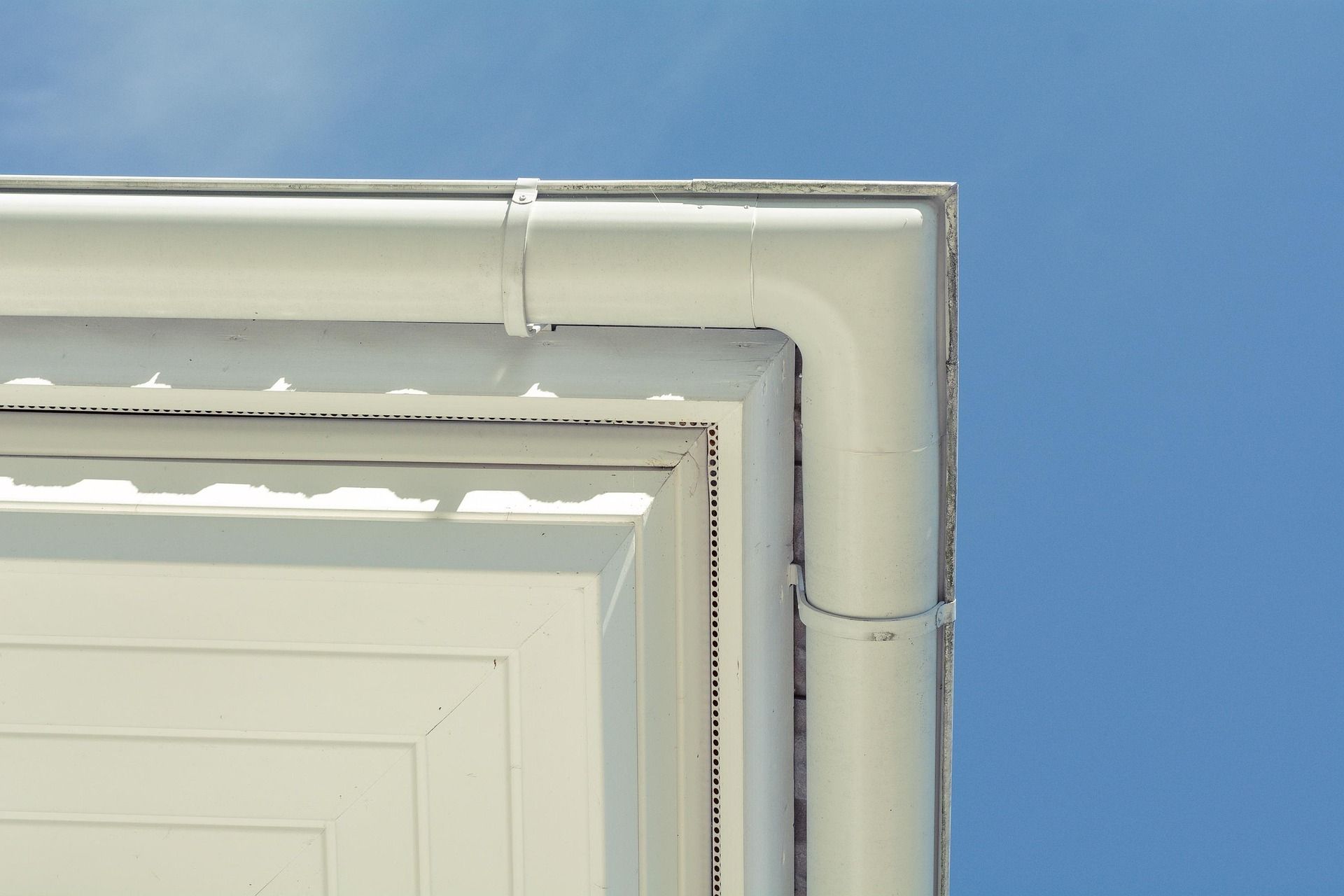 White corner of building with white gutters against a blue sky.