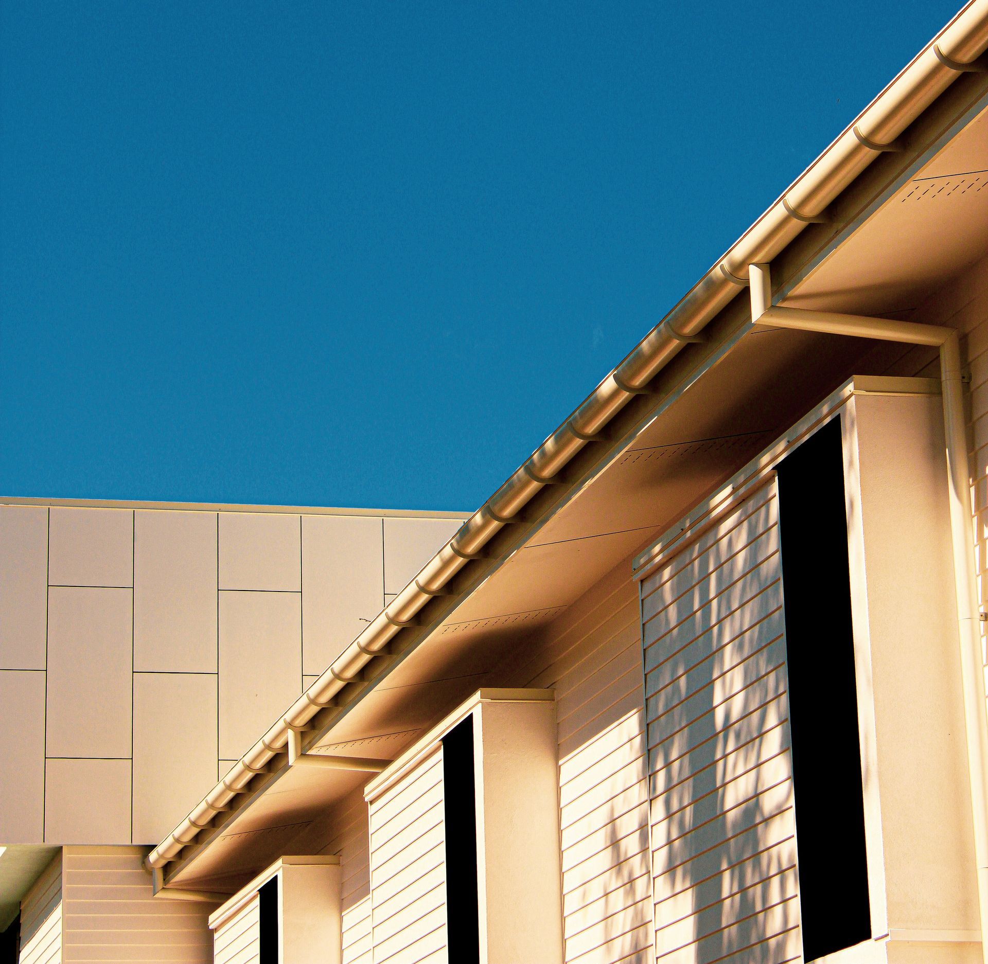 Beige building exterior with black windows, against a bright blue sky.