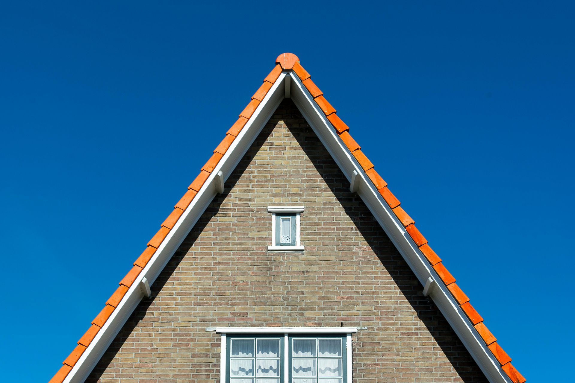 Triangular brick building gable with orange roof and a small window against a blue sky.