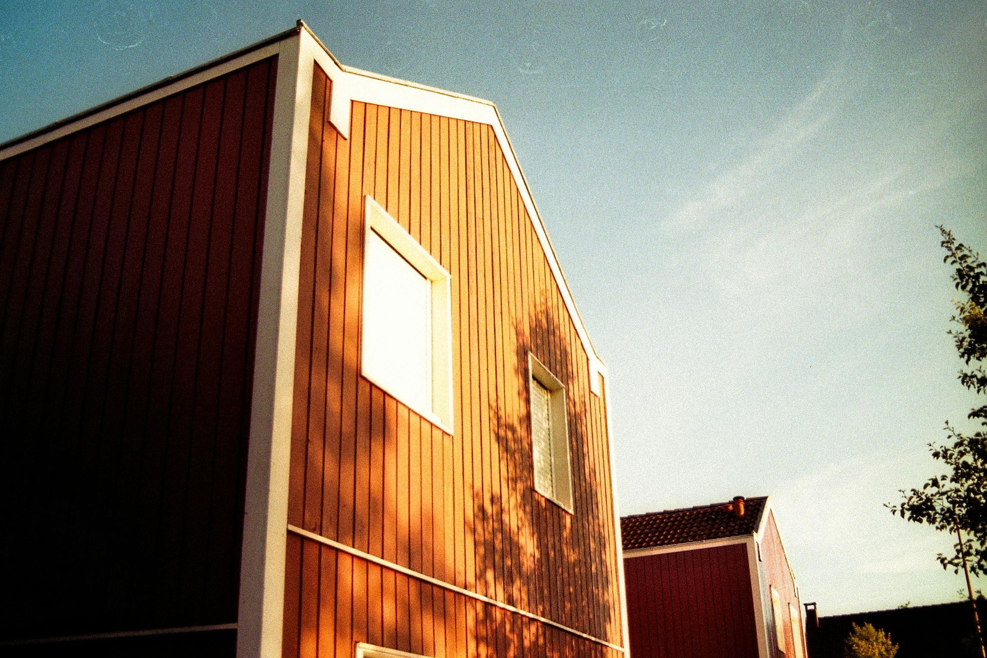 Red wooden building with white trim against a blue sky, sunlit.