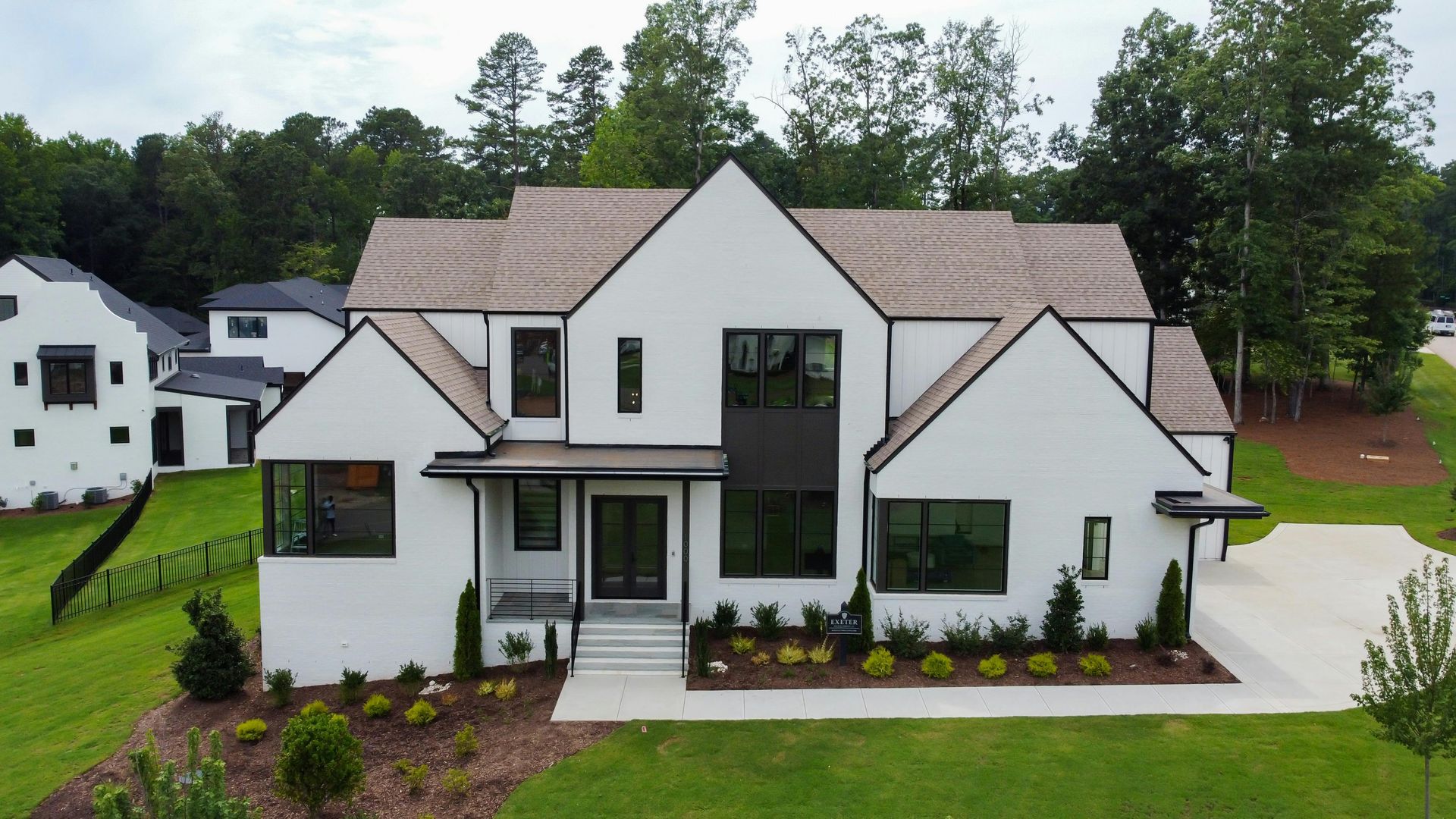White modern home with black window frames, tan roof, and green lawn.