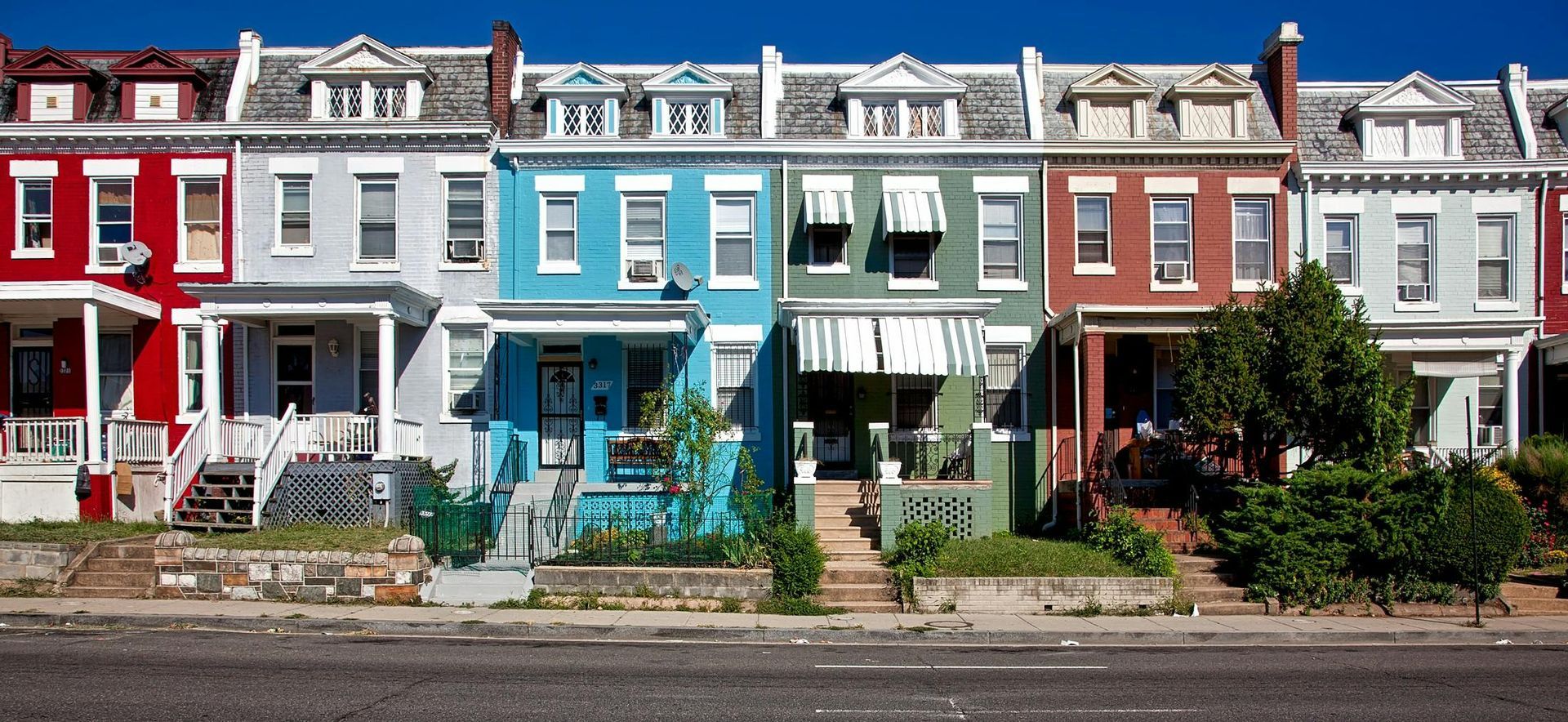 Row of colorful townhouses with porches and street in front.