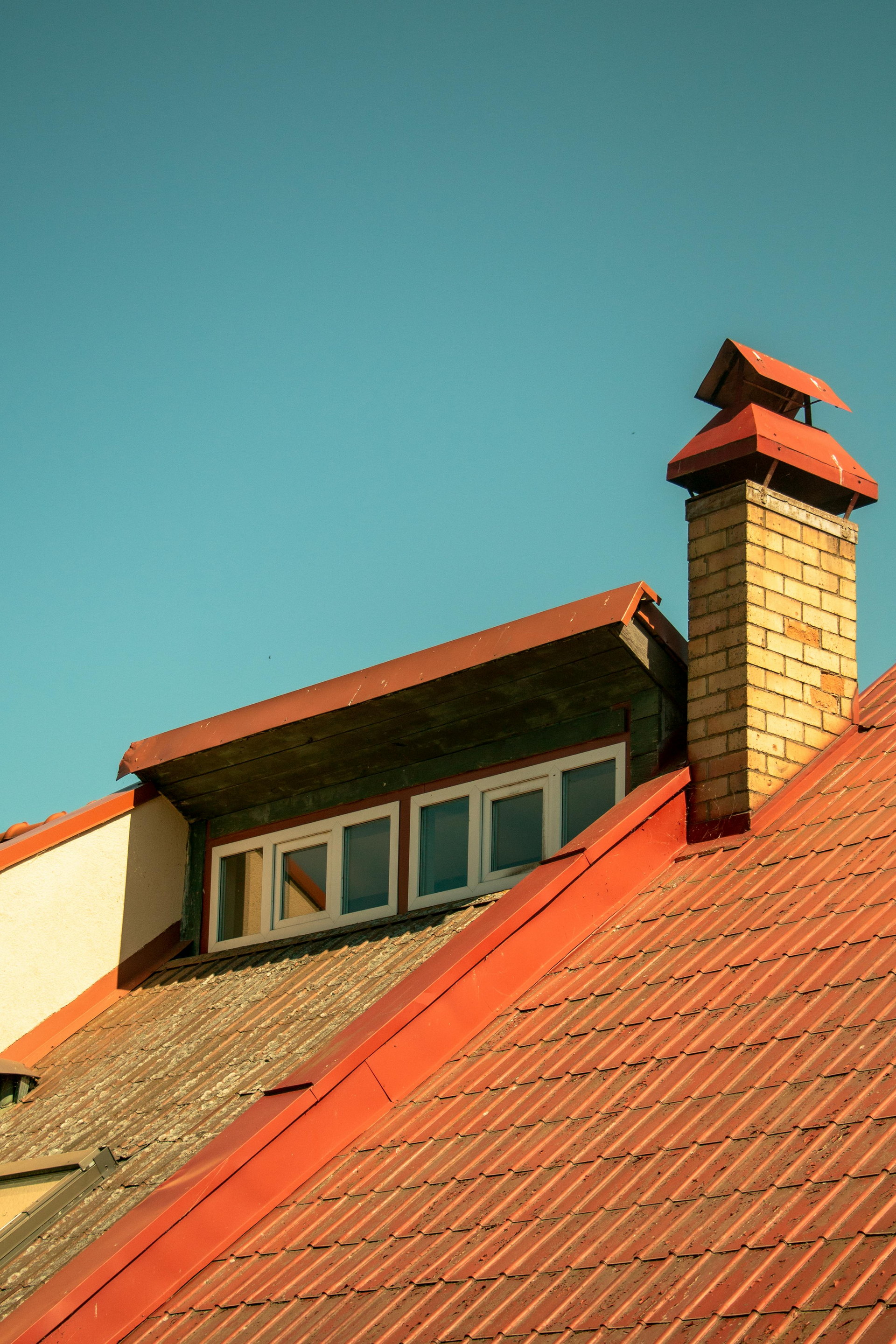 Red-tiled rooftop with dormer windows and brick chimney against a clear blue sky.