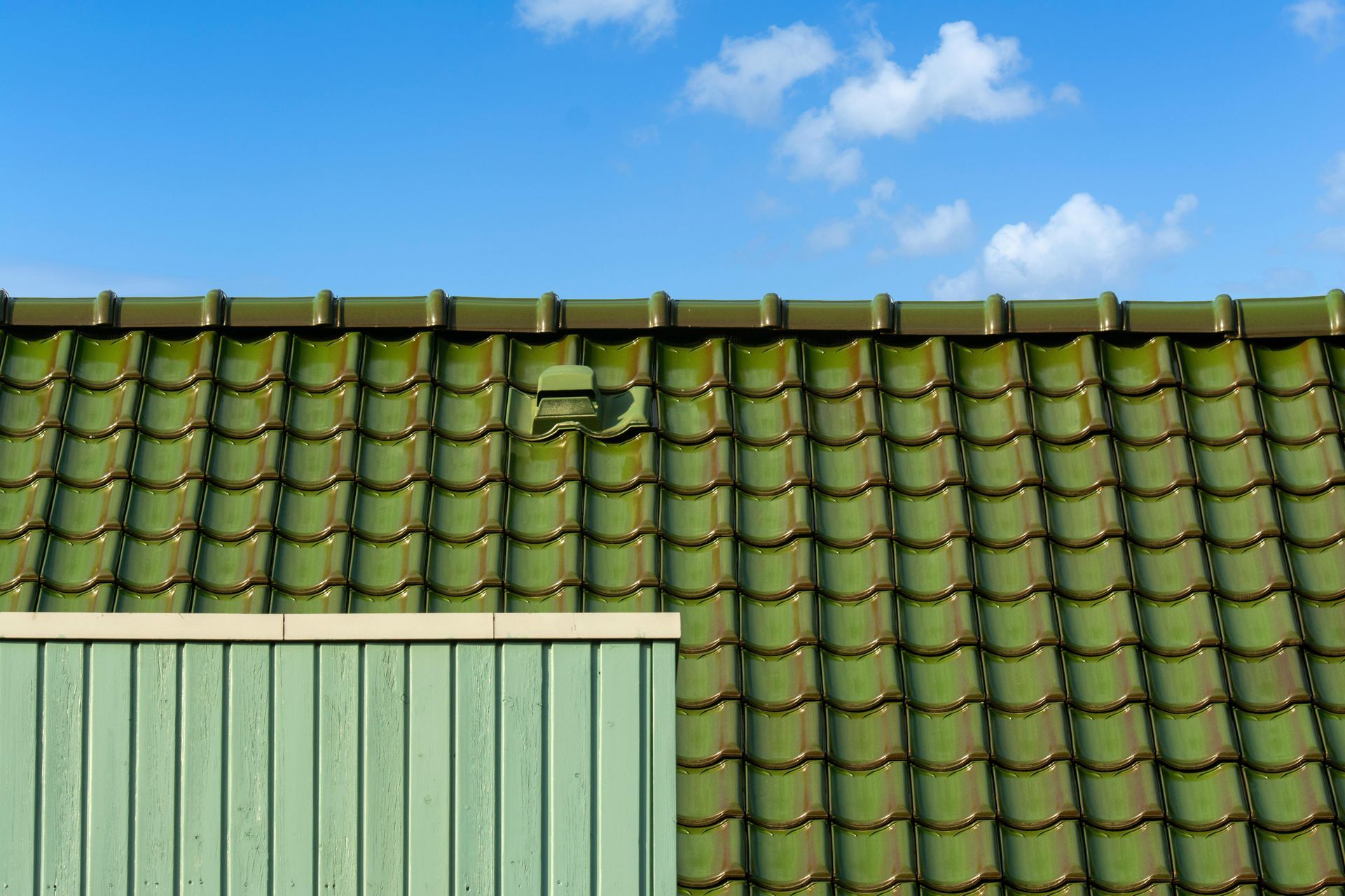 Green tiled roof and green wooden siding against a blue sky with white clouds.