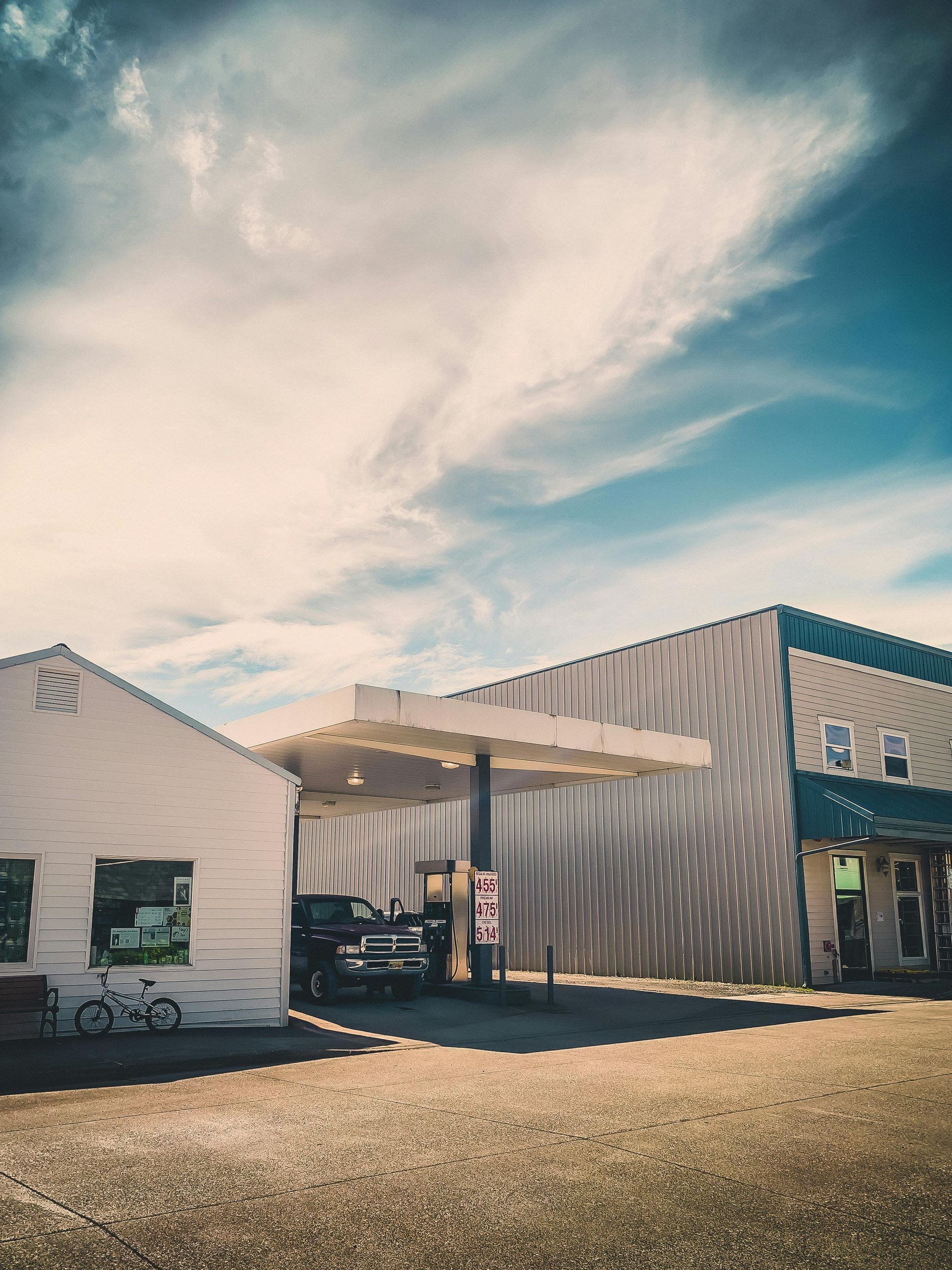 Gas station with white buildings under a blue sky with wispy clouds.