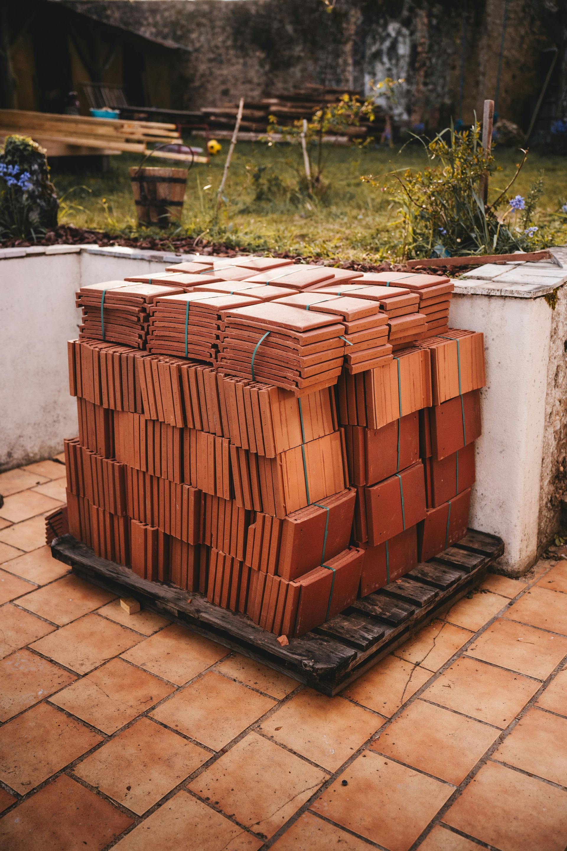 Stack of red bricks on a pallet in a backyard setting.