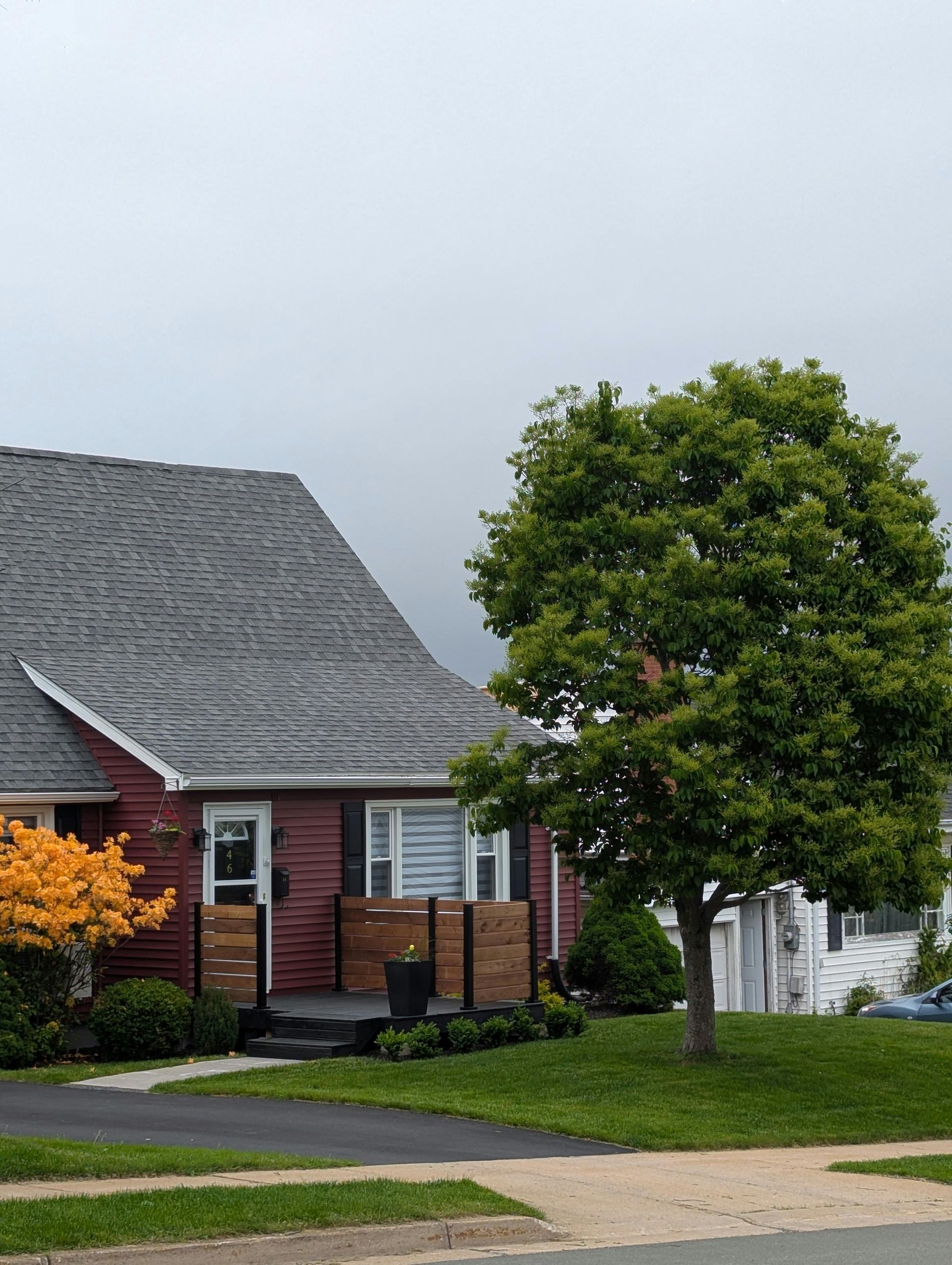 Red house with dark roof and green tree on a cloudy day.