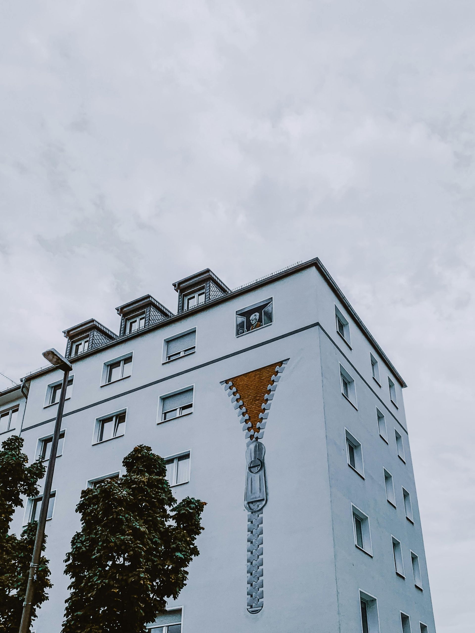 White building with mural of a gold and gray zipper partially opening a side. 