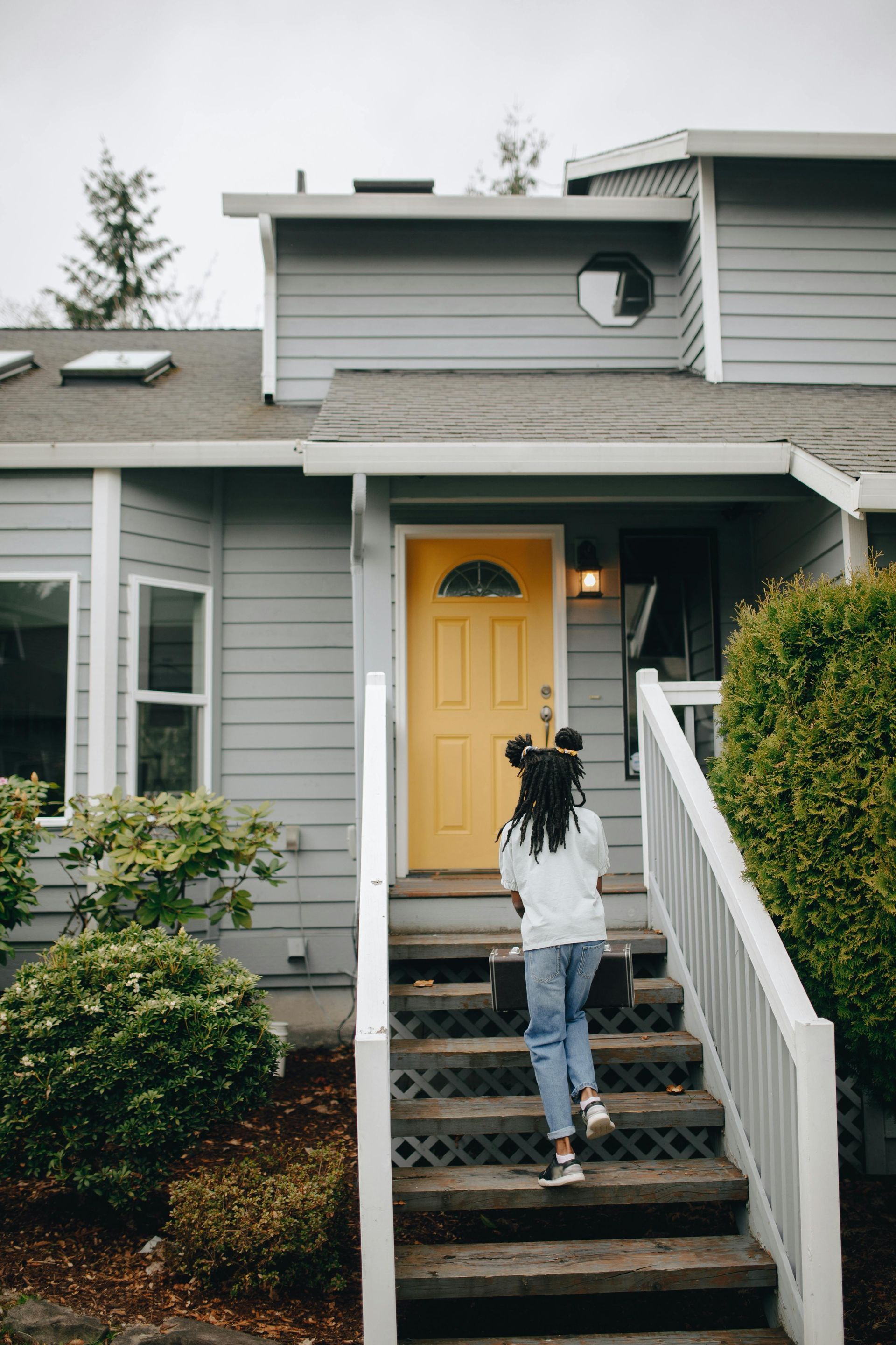 Girl ascending wooden stairs towards a house with a yellow door.