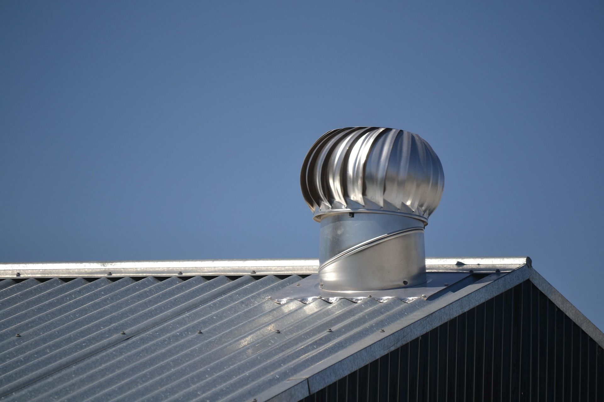 A metal wind turbine on a corrugated metal roof against a clear blue sky.