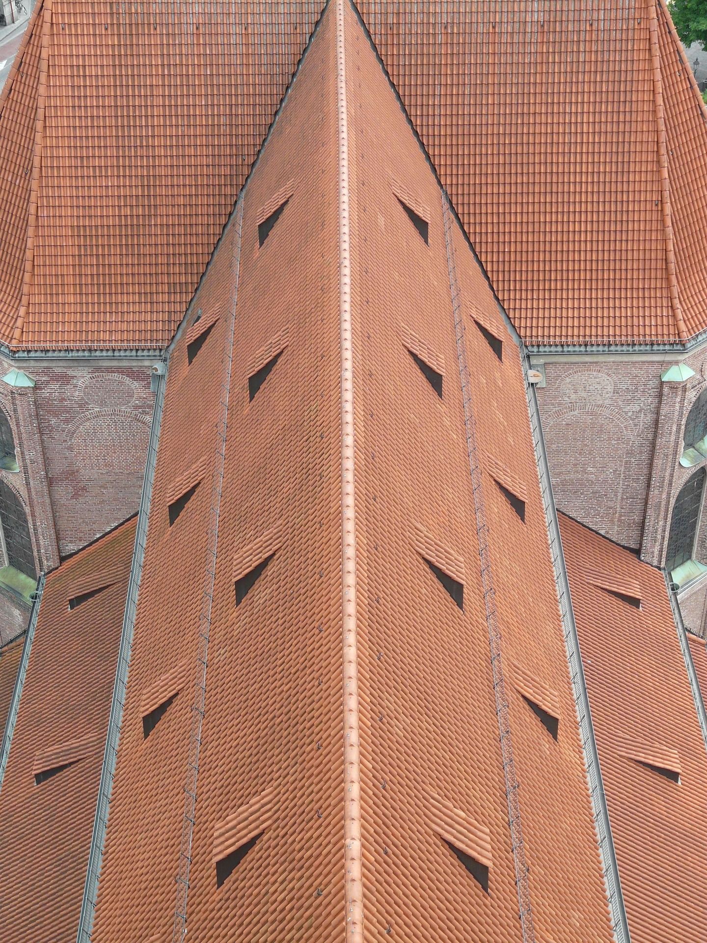 Overhead view of a terracotta-tiled church roof with triangular ventilation openings.