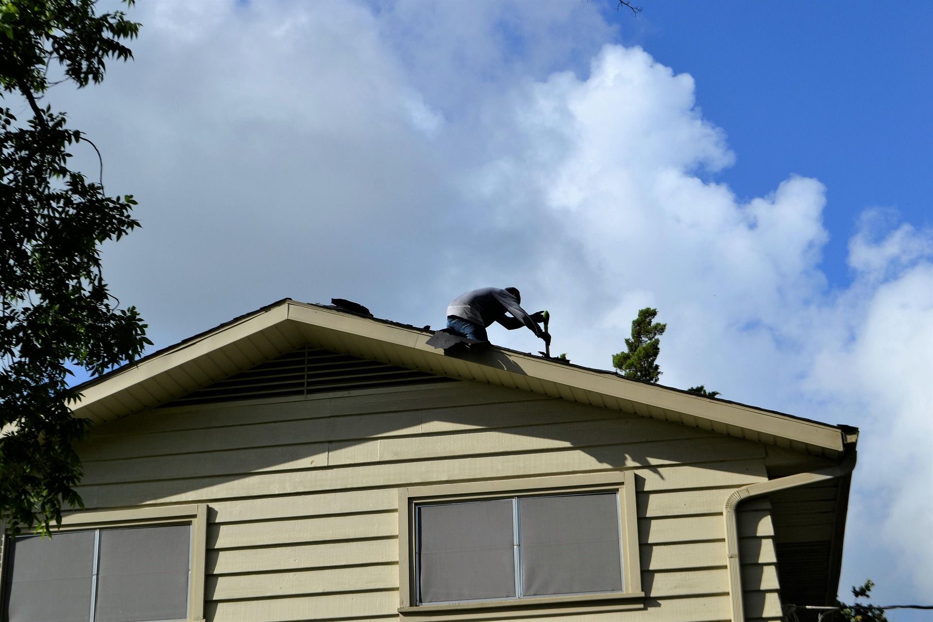 Person on a roof working, with a drill, cloudy blue sky background.