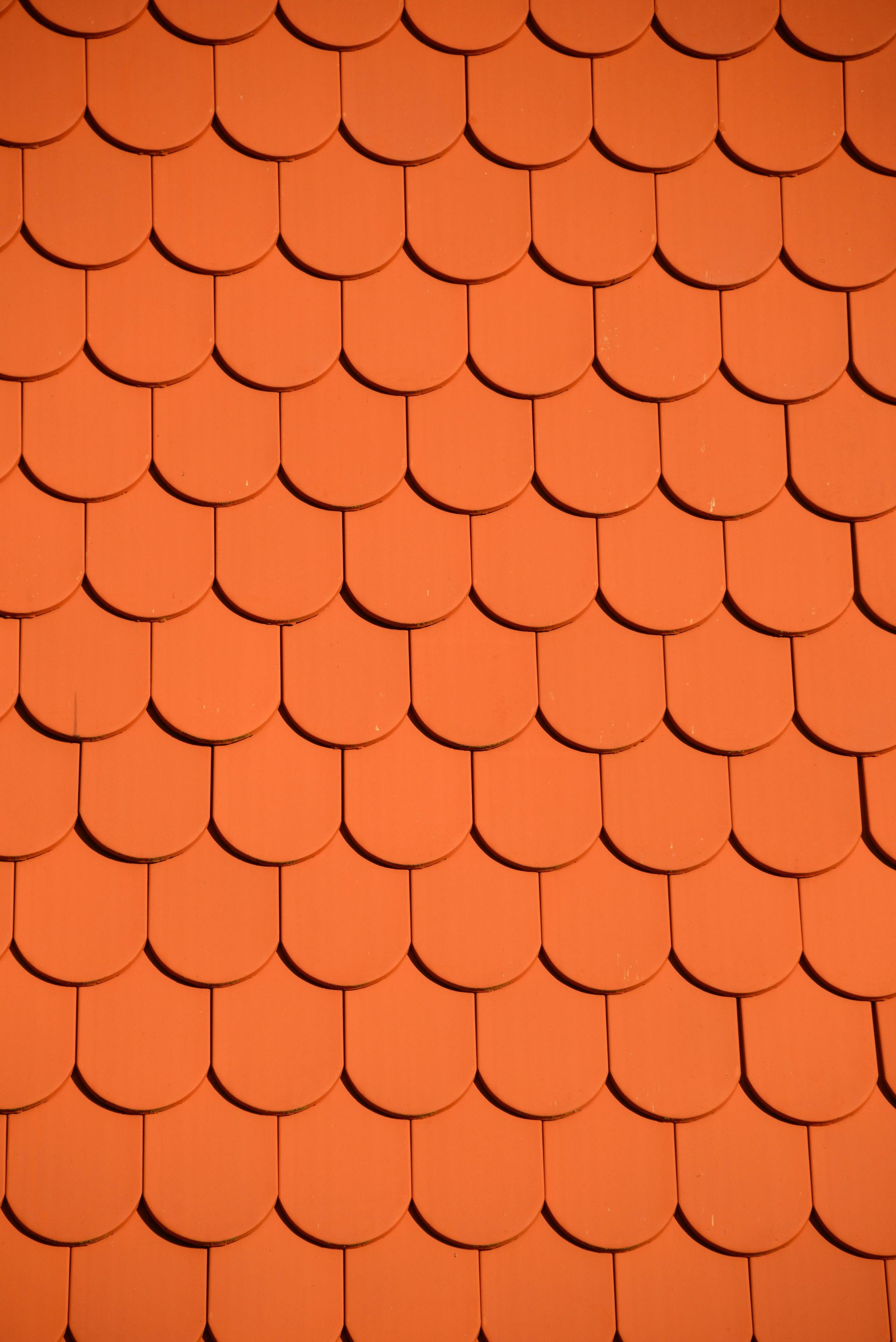 Orange, scallop-shaped roof tiles arranged in a grid pattern, casting shadows.