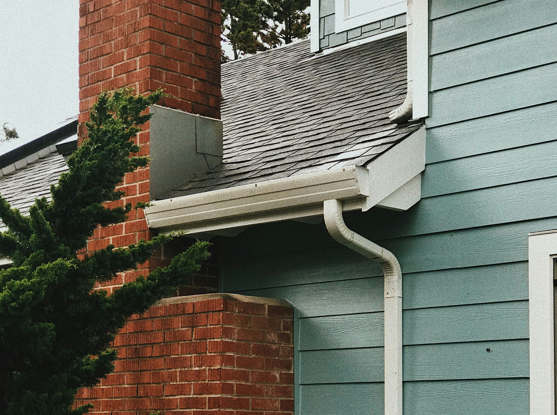 Brick chimney and blue house with white trim; rain gutter.