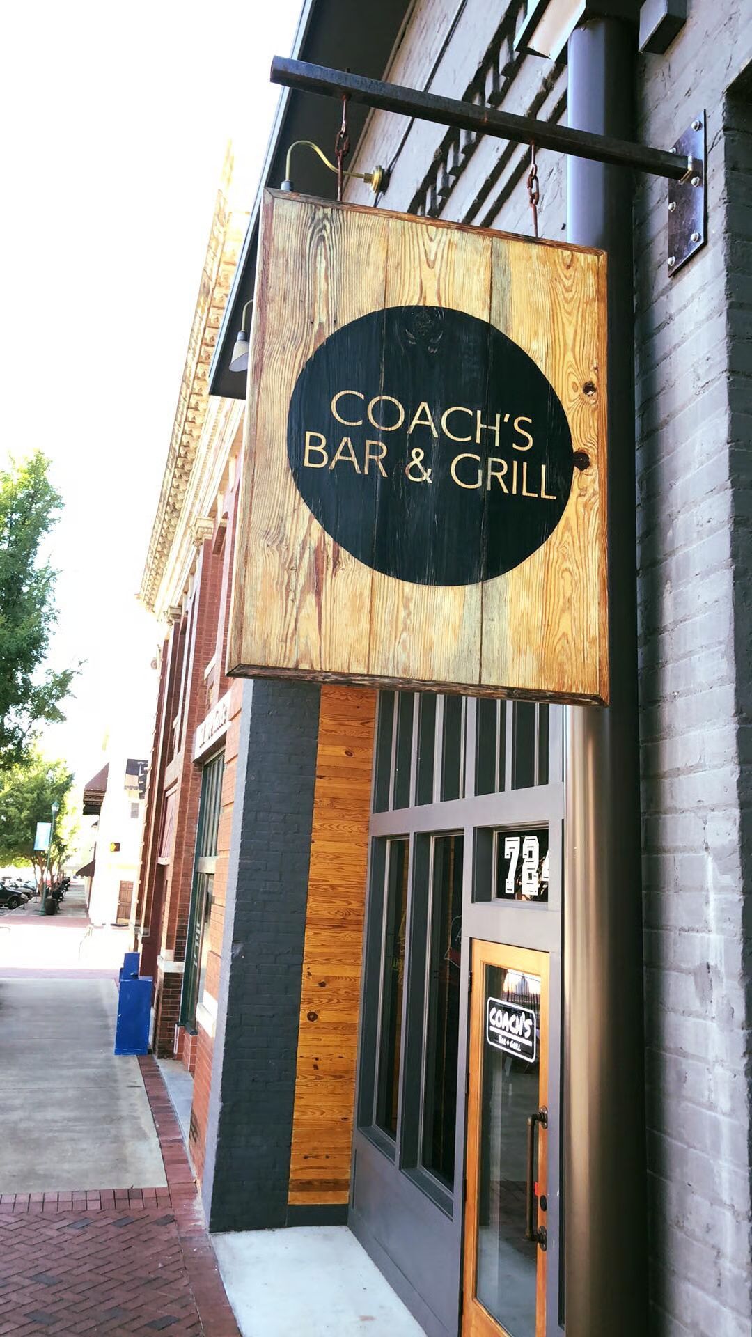Coach's Bar & Grill sign; weathered wooden sign with black circle and lettering; building facade.