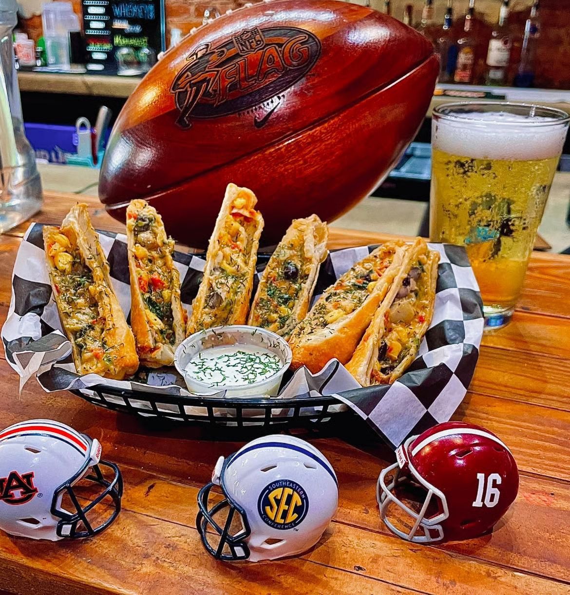 Appetizers, beer, and football helmets on a bar. A wooden football is behind the food.
