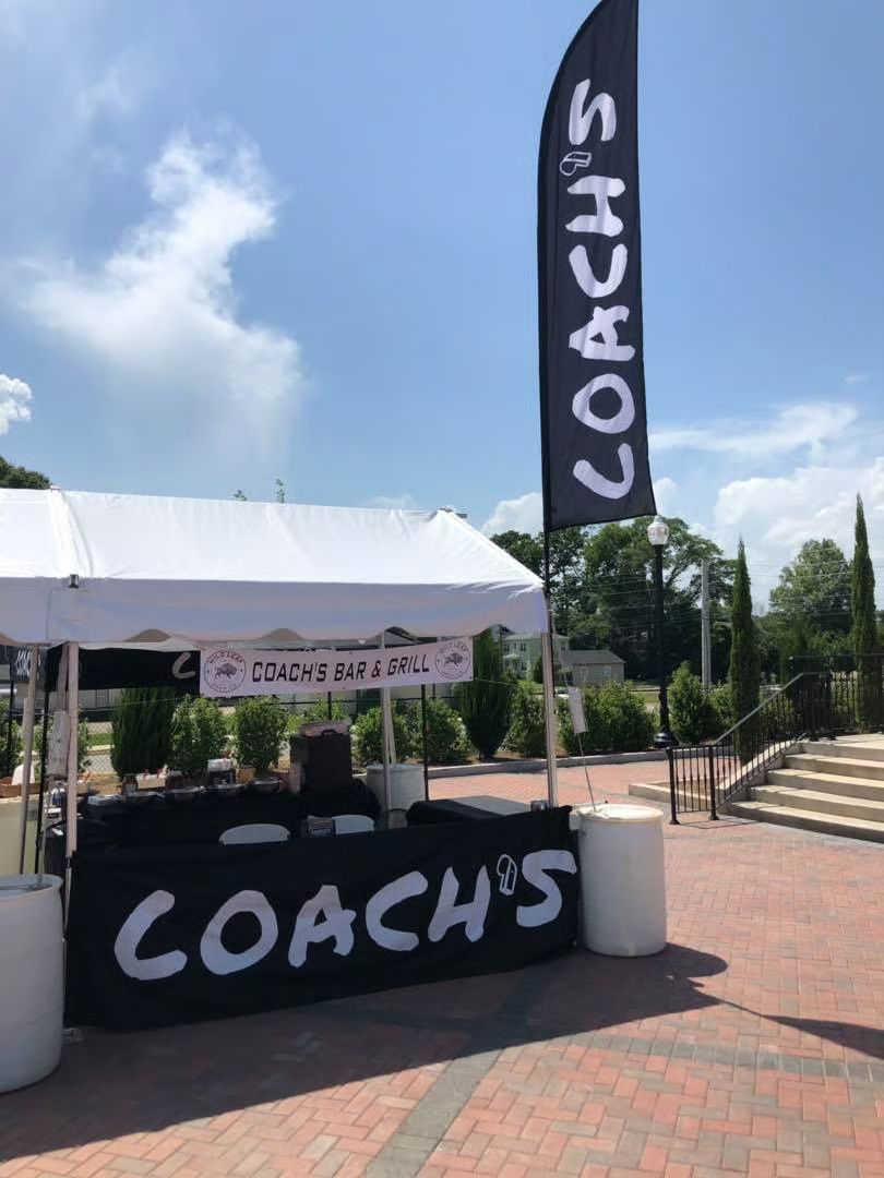 Coach's food stall with black and white branding, set up outdoors under a blue sky.