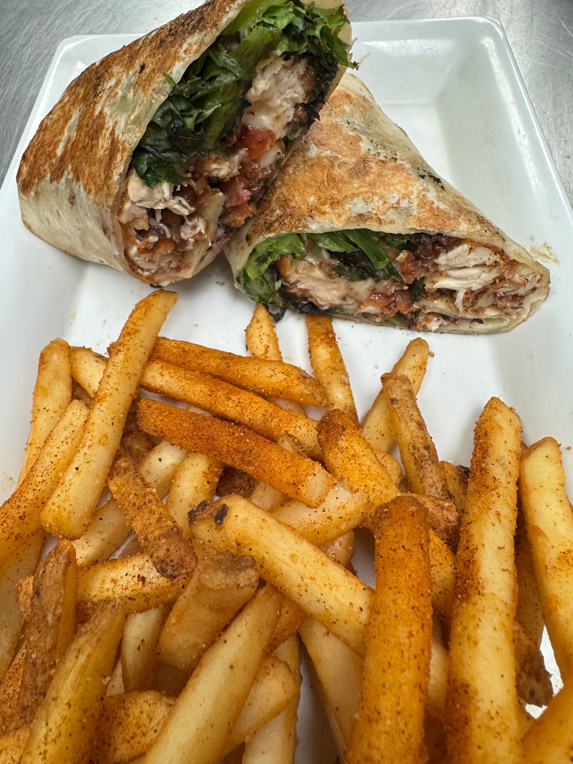 Chicken wrap and seasoned fries on a white plate.