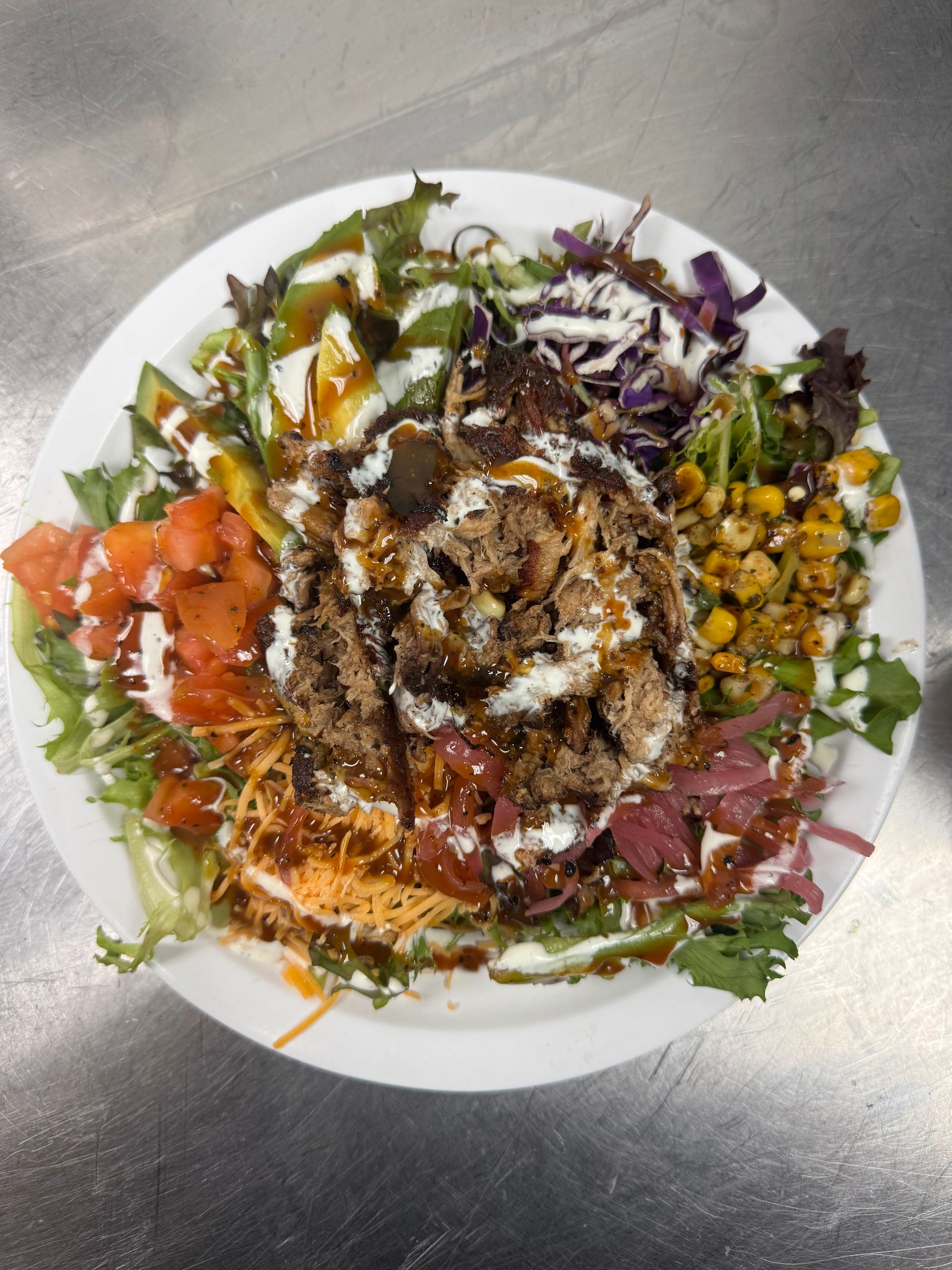 Salad bowl with various colorful toppings, drizzled with sauces, on a white plate.