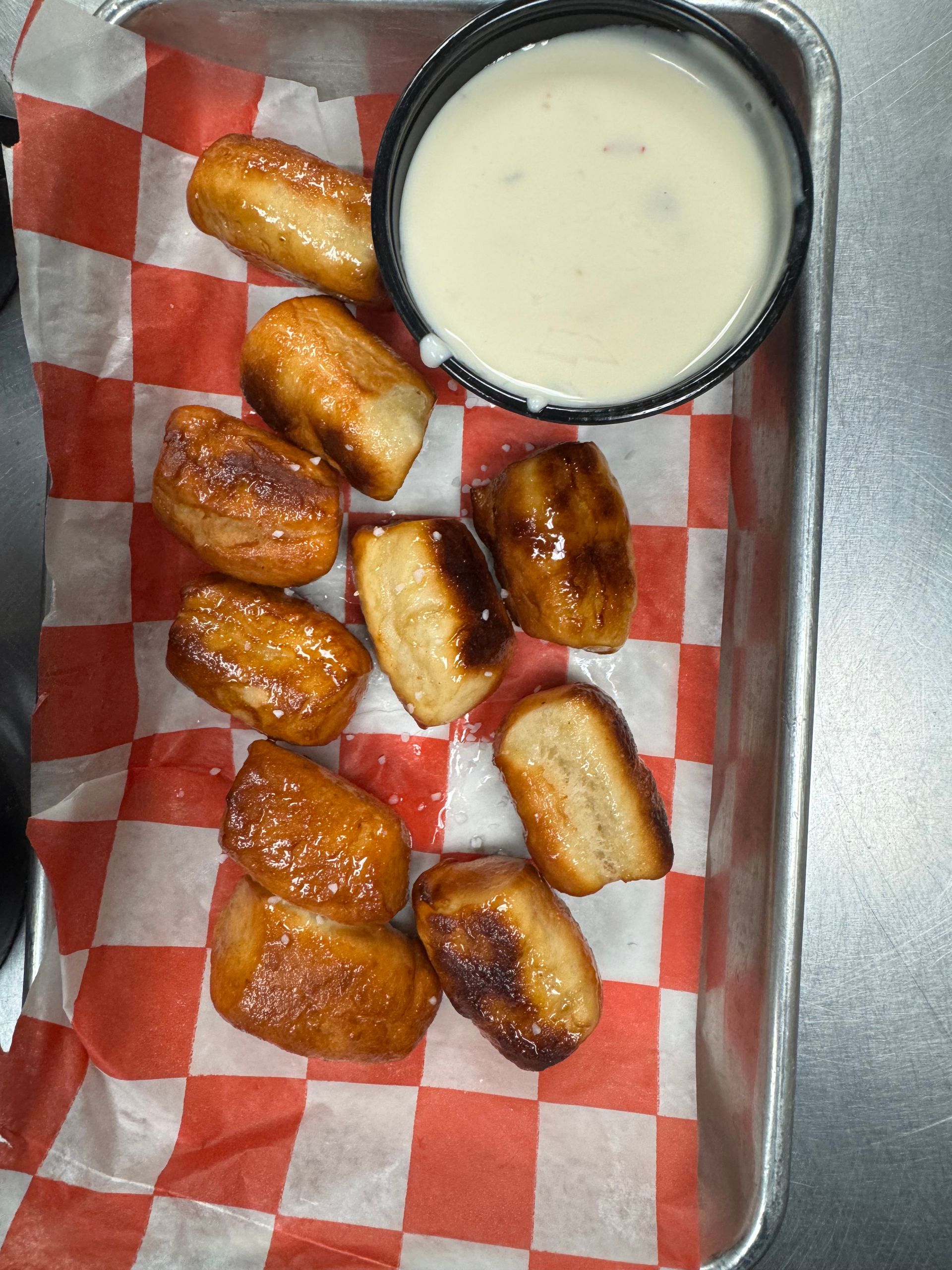Pretzel bites with white dipping sauce in a tray lined with red and white checkered paper.