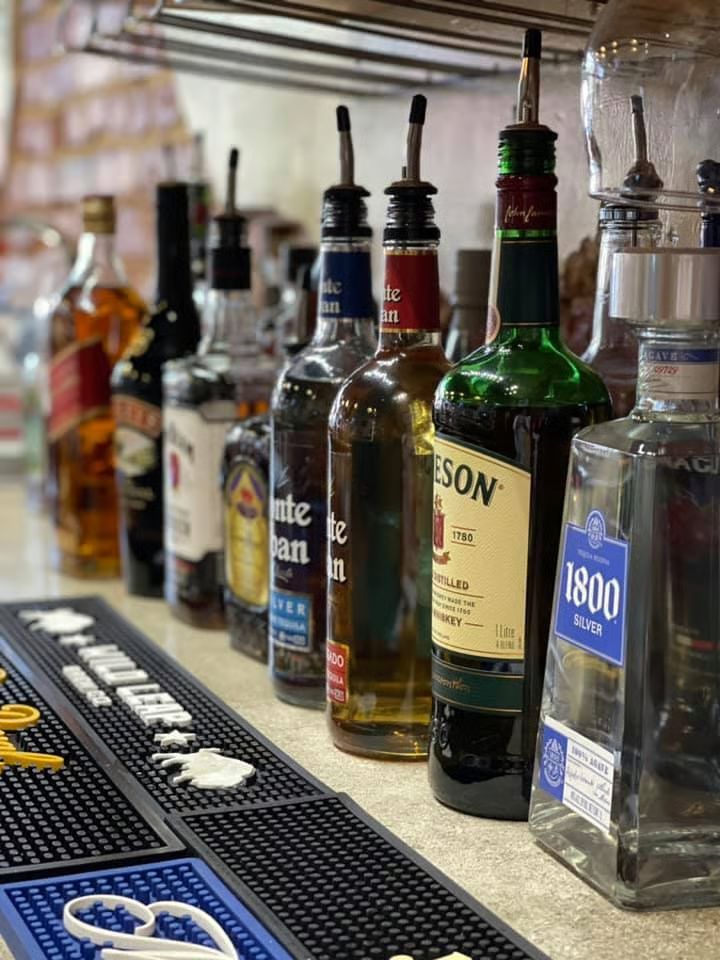 Liquor bottles with pour spouts on a bar, various brands and colors.