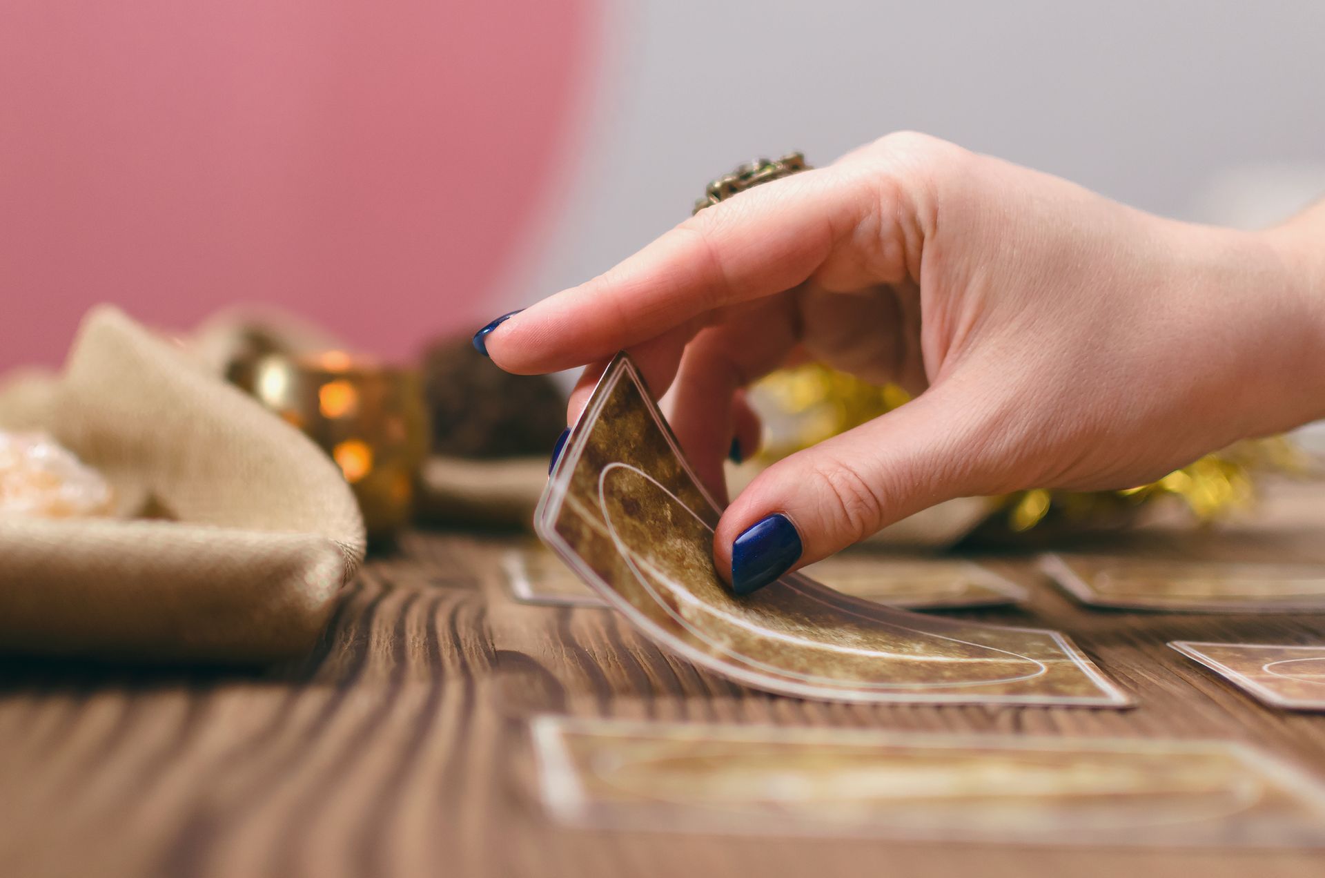 Woman's hand with dark nails picks a tarot card from a spread on a wooden table.