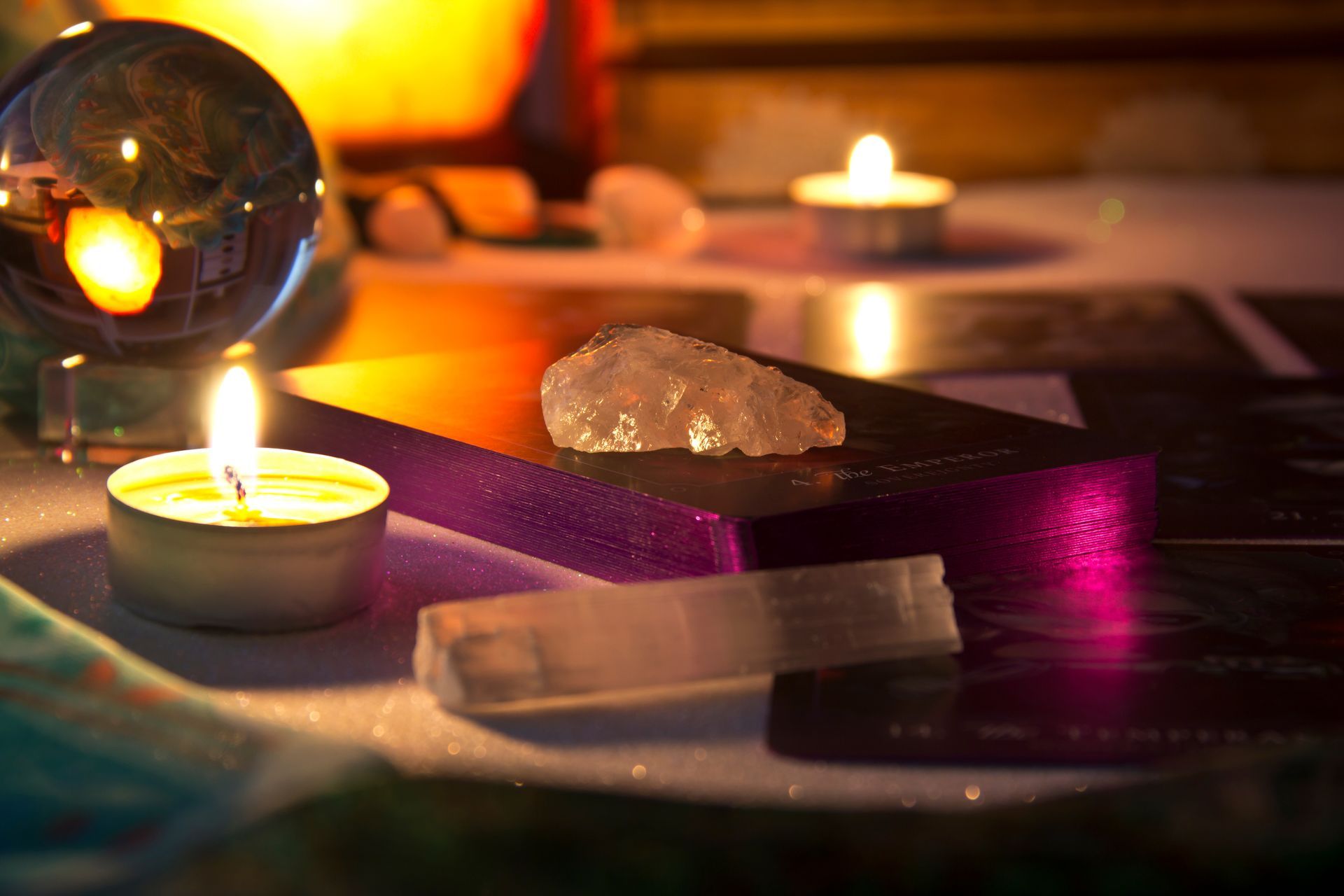 Lit candles with a crystal ball, crystals, and tarot cards on a table. Glowing, soft lighting.