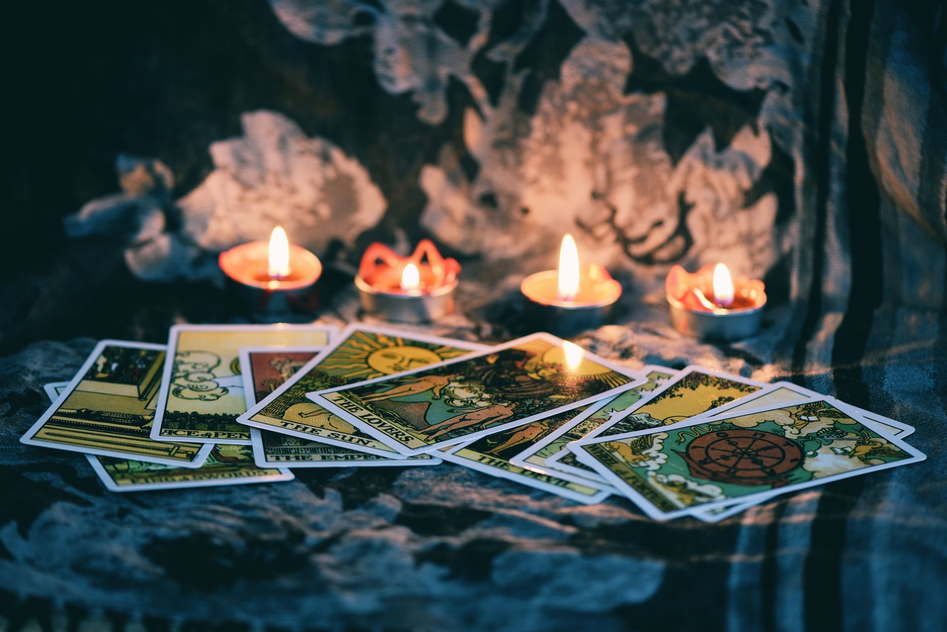 Tarot cards fanned out, lit by candles on a floral fabric. Dark, intimate setting.