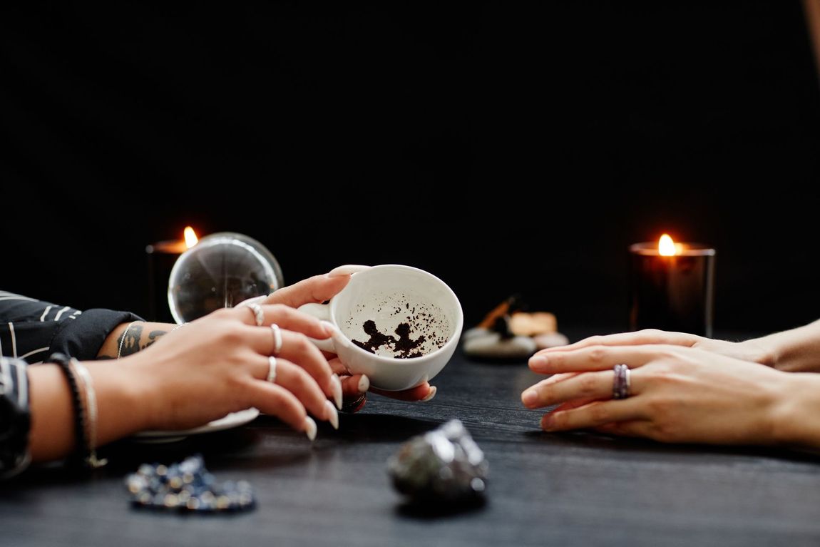 Hands holding a coffee cup with grounds, used for fortune telling, with candles, crystals, and a crystal ball.