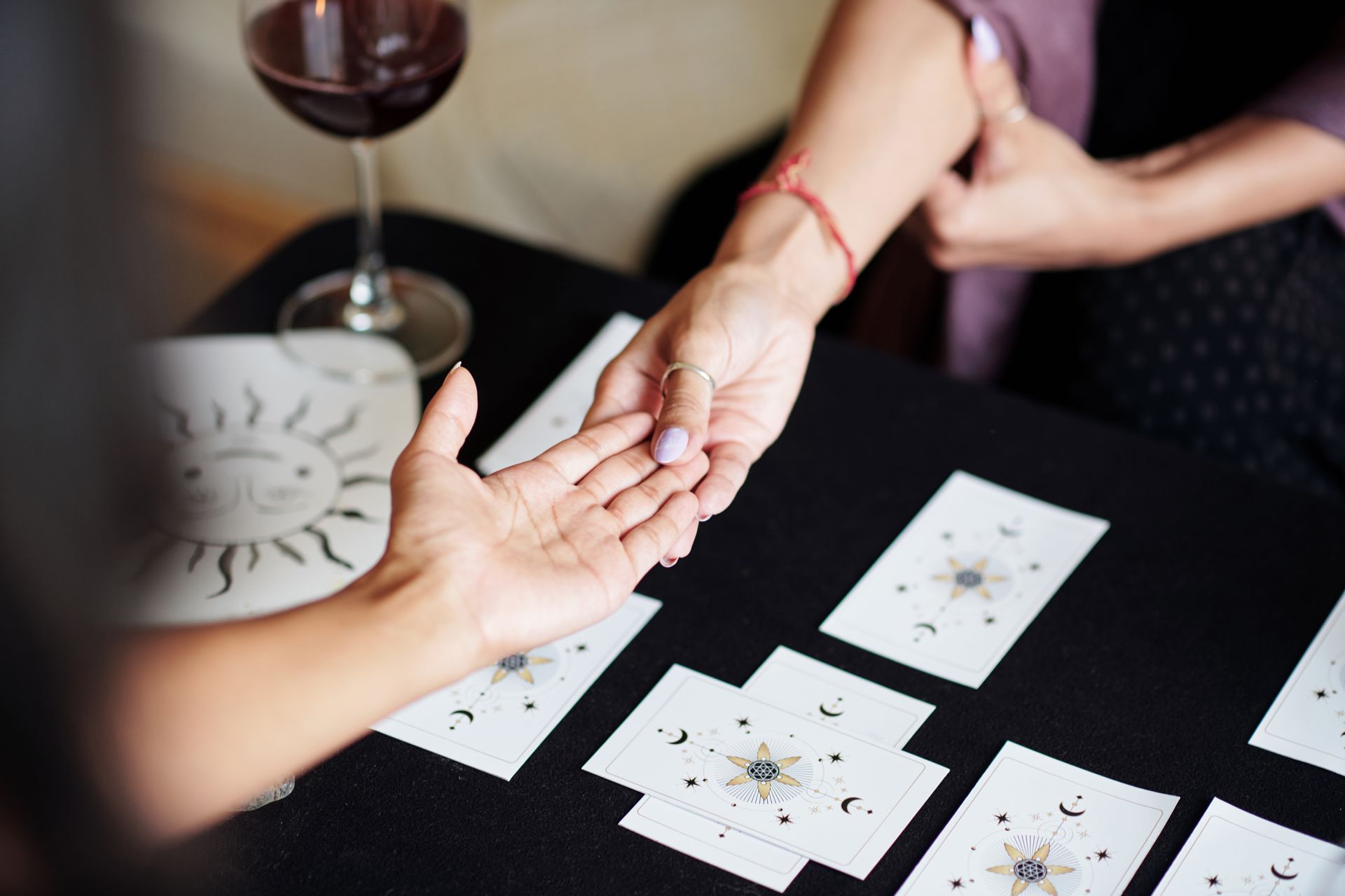 Palm reading session, person holding another's hand over cards, glass of wine on a table.
