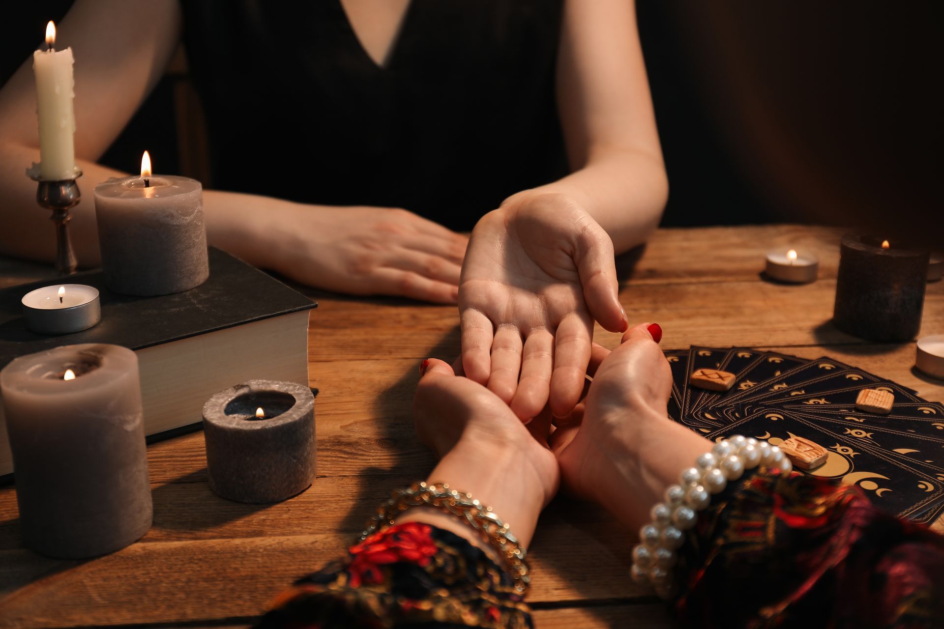 Person's palm being read at table with candles, a book, and jewelry.