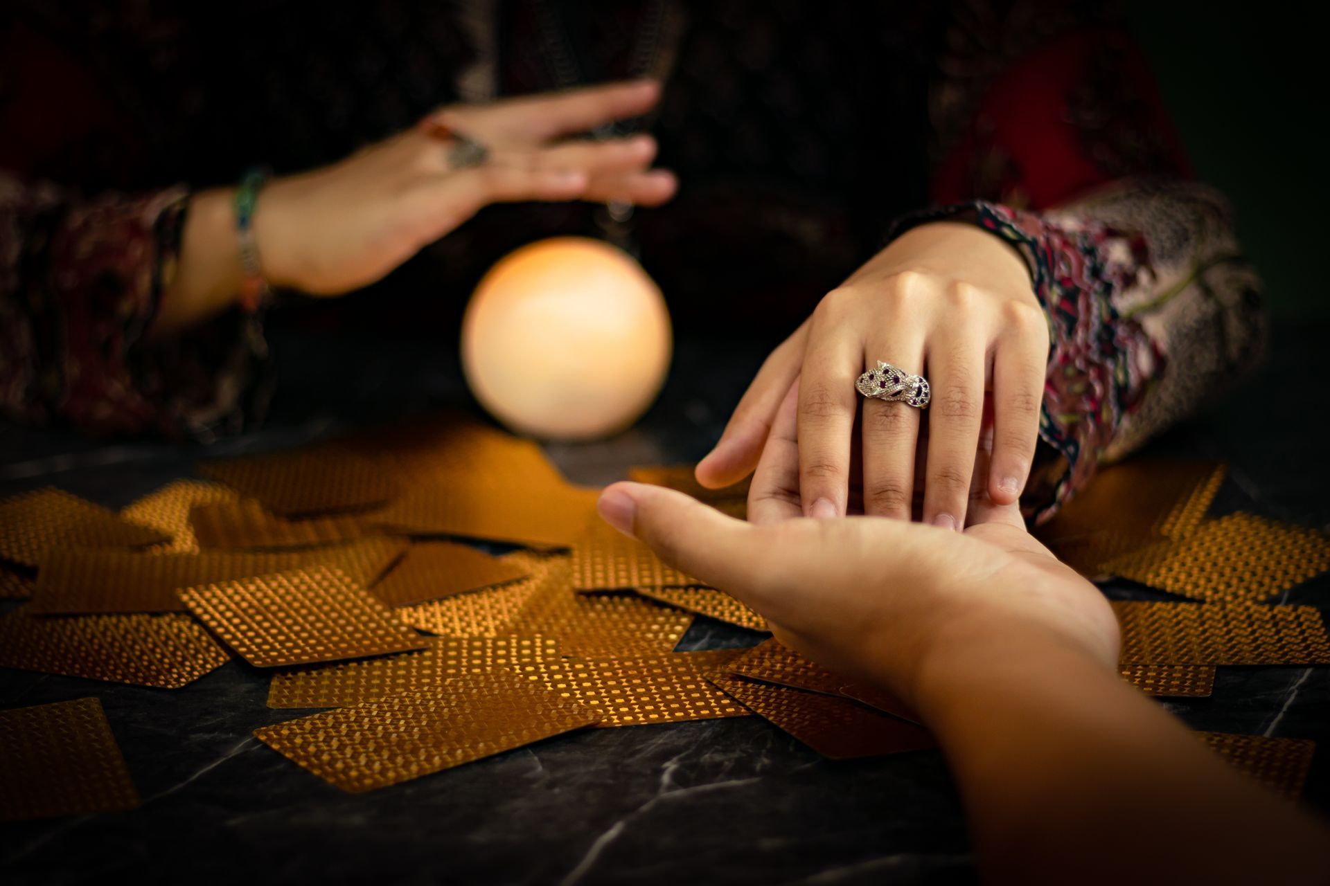 Palm reading: hands, crystal ball, tarot cards on a dark surface, with soft lighting.