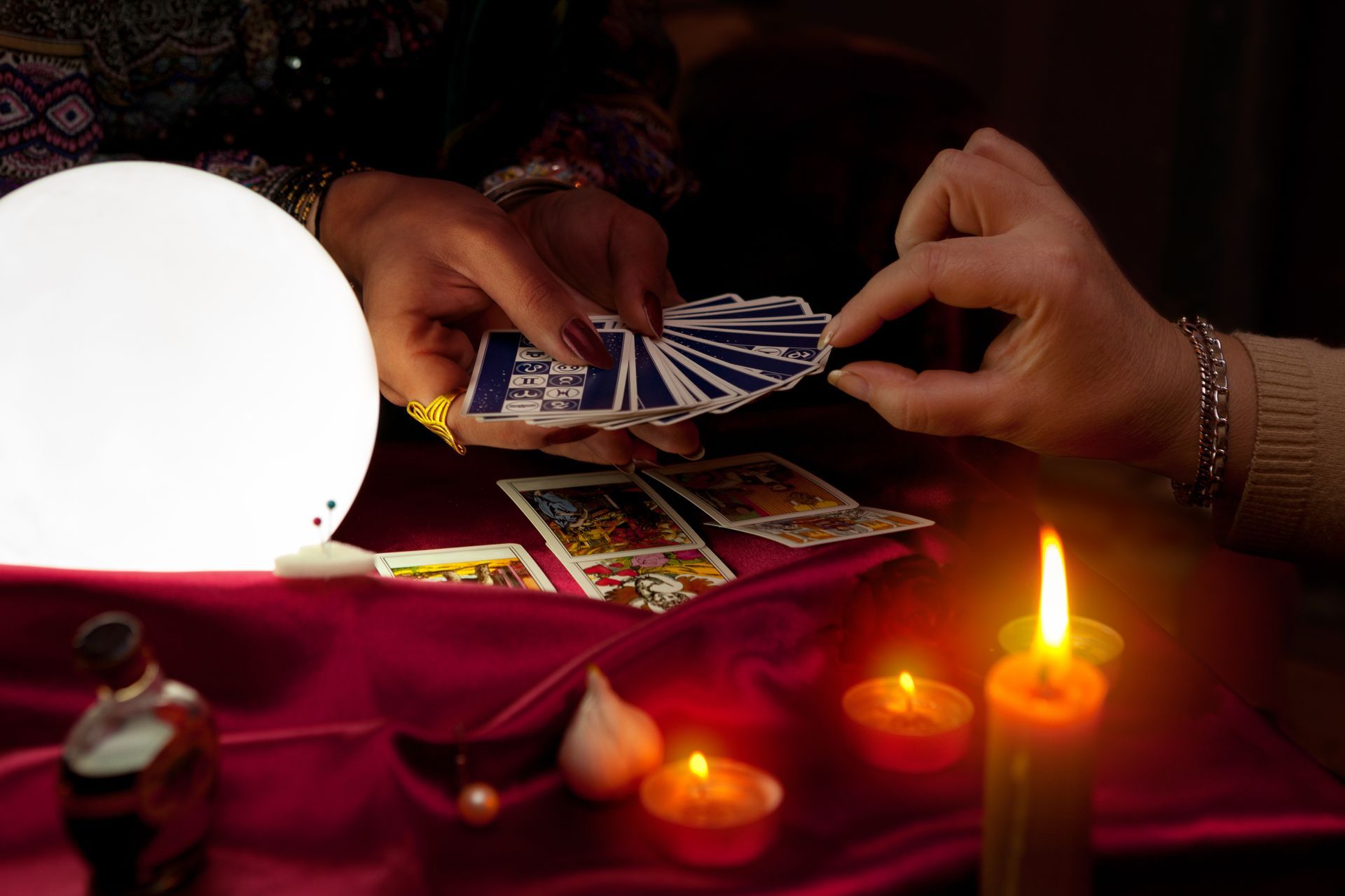 Hands shuffling tarot cards near candles and crystal ball.