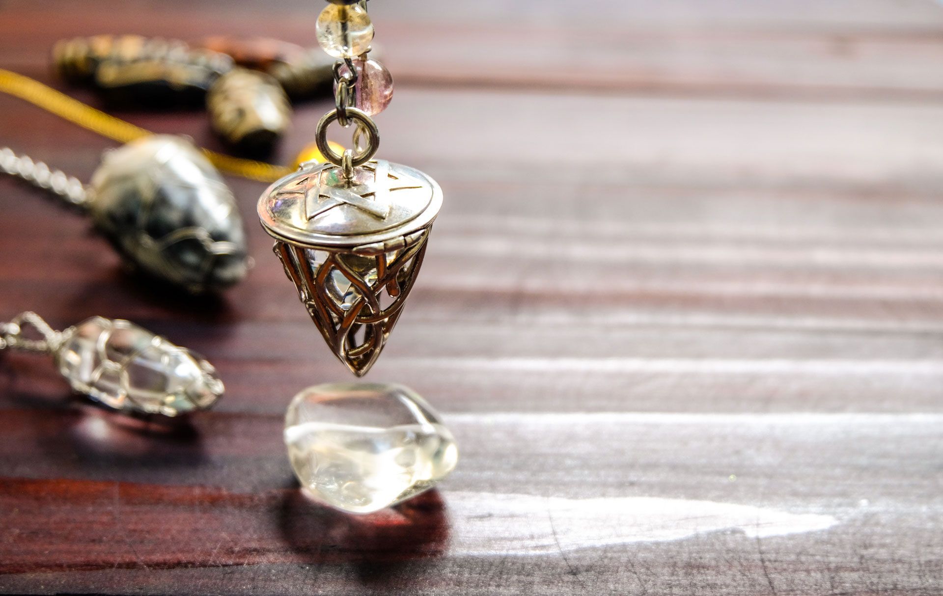 Close-up of a decorative pendulum with crystals on a wooden surface.