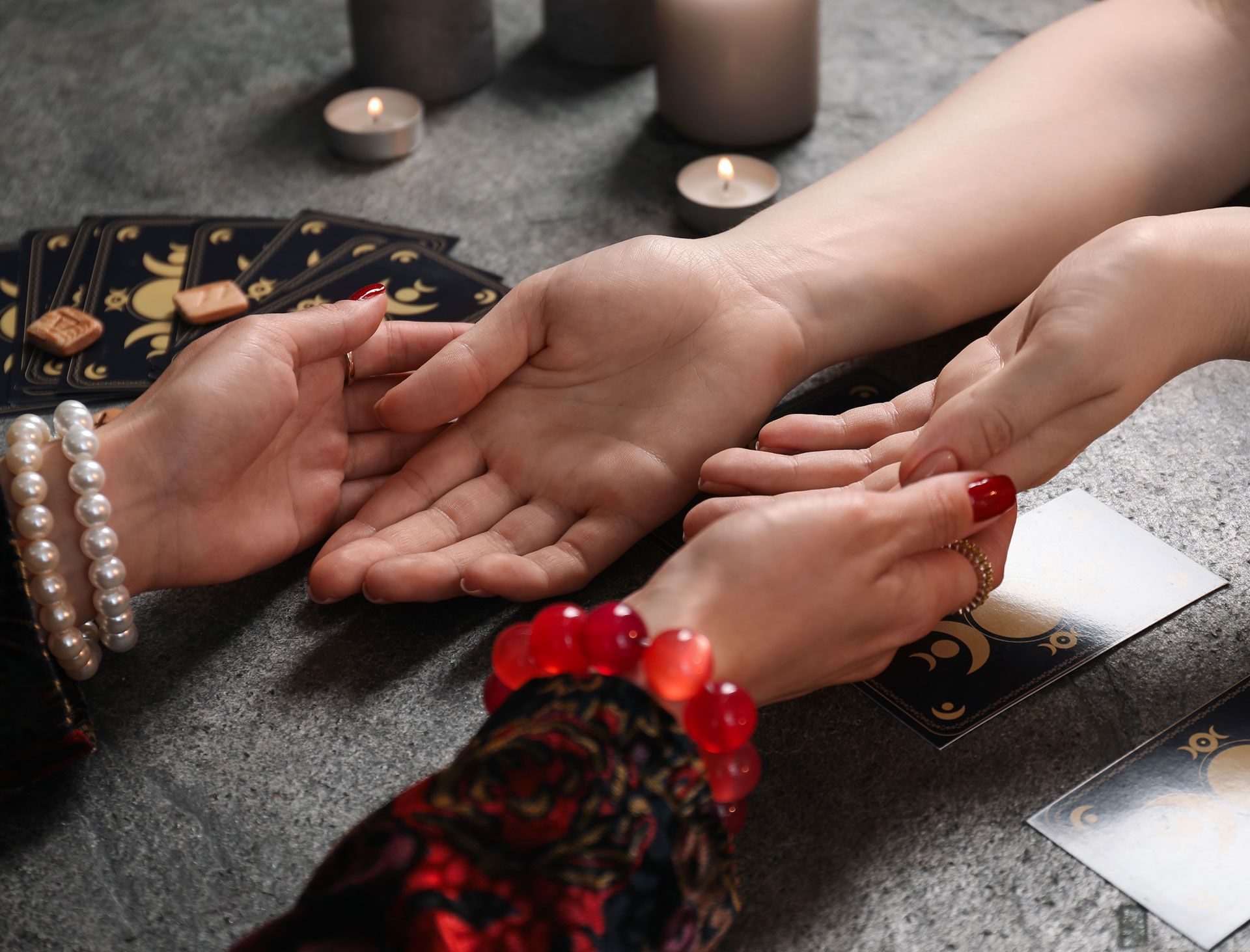 Hands being read by palm reader with tarot cards and candles.
