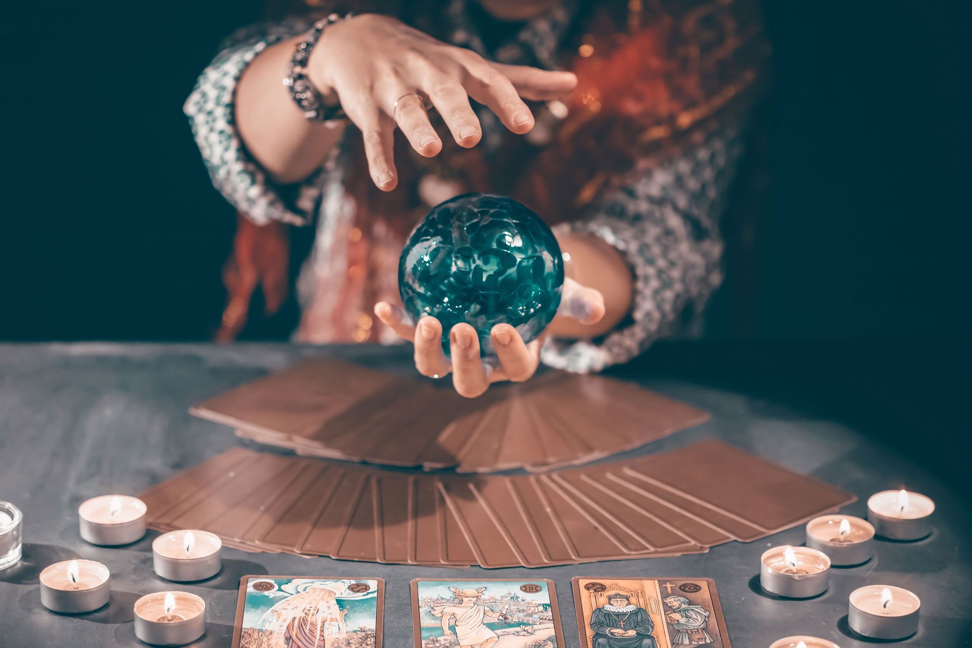 Hands hovering over a crystal ball, surrounded by lit candles and tarot cards.