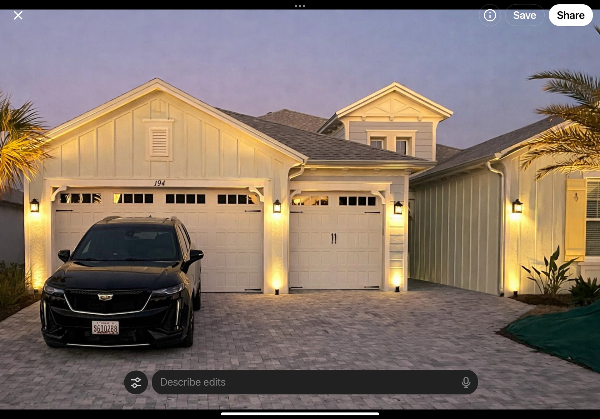 Black Cadillac SUV parked in front of a modern house with a white garage and exterior lighting.
